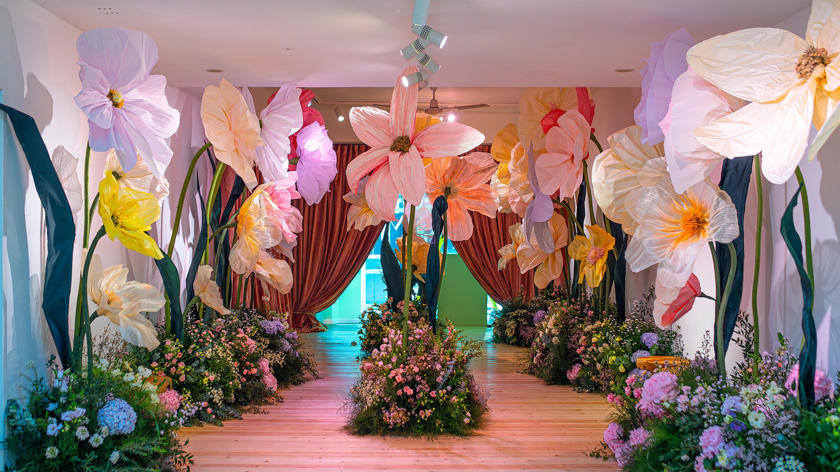 Immersive bespoke floral installation featuring oversized paper flowers and naturalistic ground arrangements creating fantastical walkway, showcasing Amaranté London's artistic approach to original custom floral design for extraordinary event experiences - Amarante London
