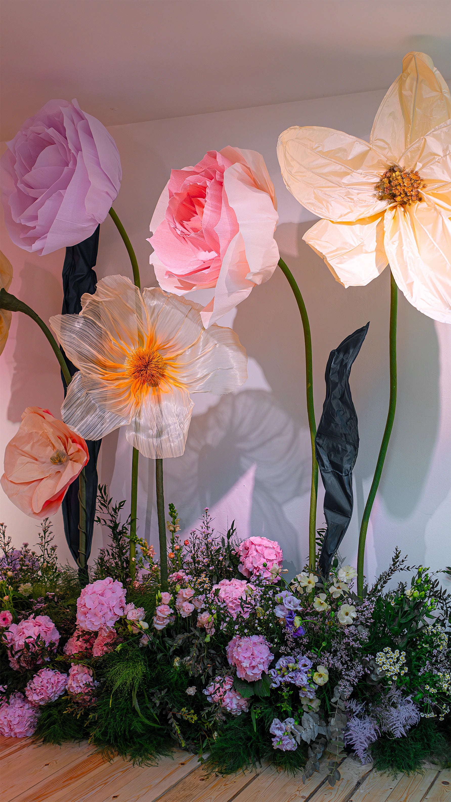 Immersive bespoke floral installation featuring oversized paper flowers and naturalistic ground arrangements creating fantastical walkway, showcasing Amaranté London's artistic approach to original custom floral design for extraordinary event experiences - Amarante London