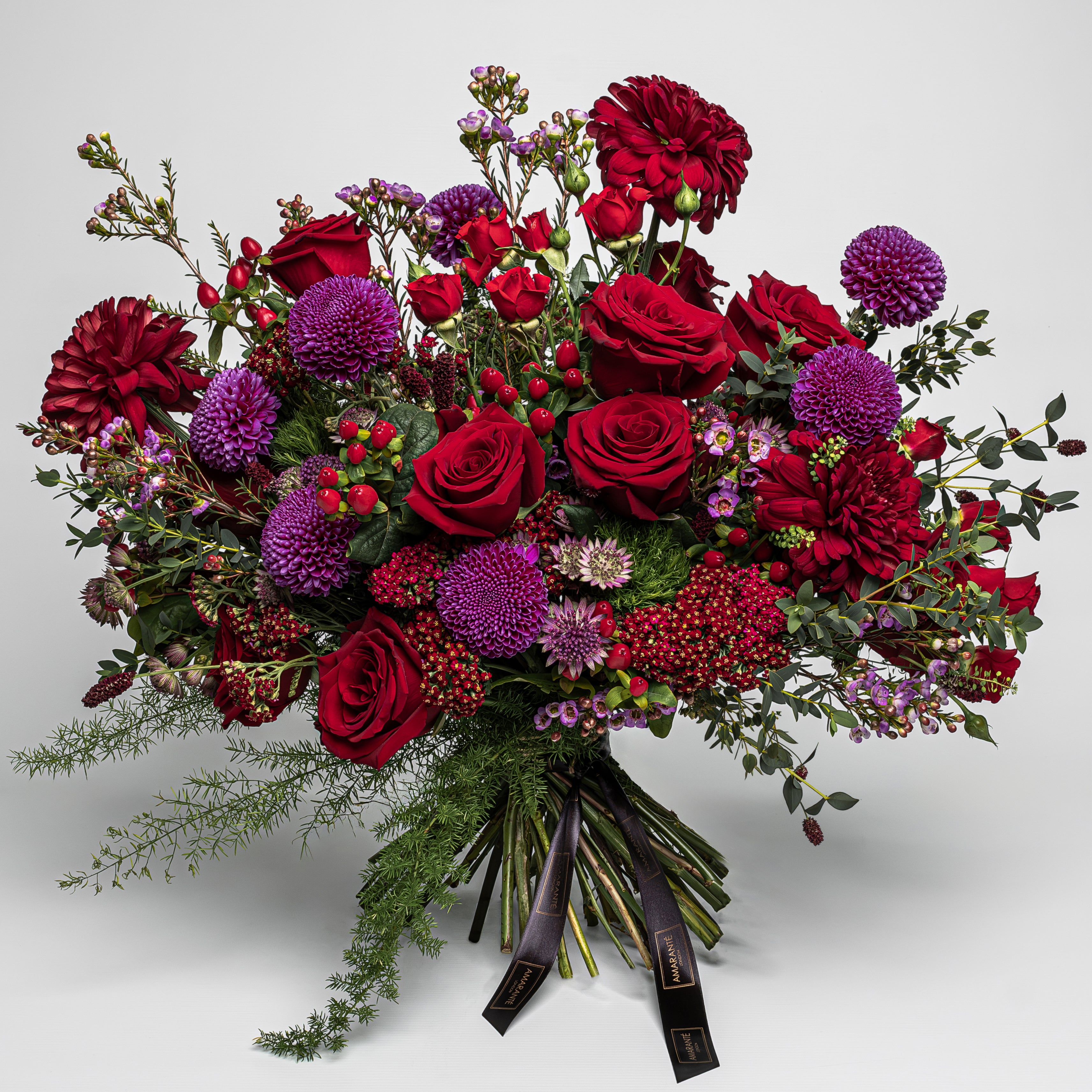Crimson Lust Fresh Flower Bouquet features deep reds and rich purples, each flower meticulously selected to create a luxurious tapestry ideal for International Women's Day and Mother's Day, Valentine's Day and other important moments. This luxury floral arrangement is dominated by the romantic allure of velvety red roses, their full blooms symbolising love and respect. Dark red dahlias add a lush, textural contrast with their intricate petals.