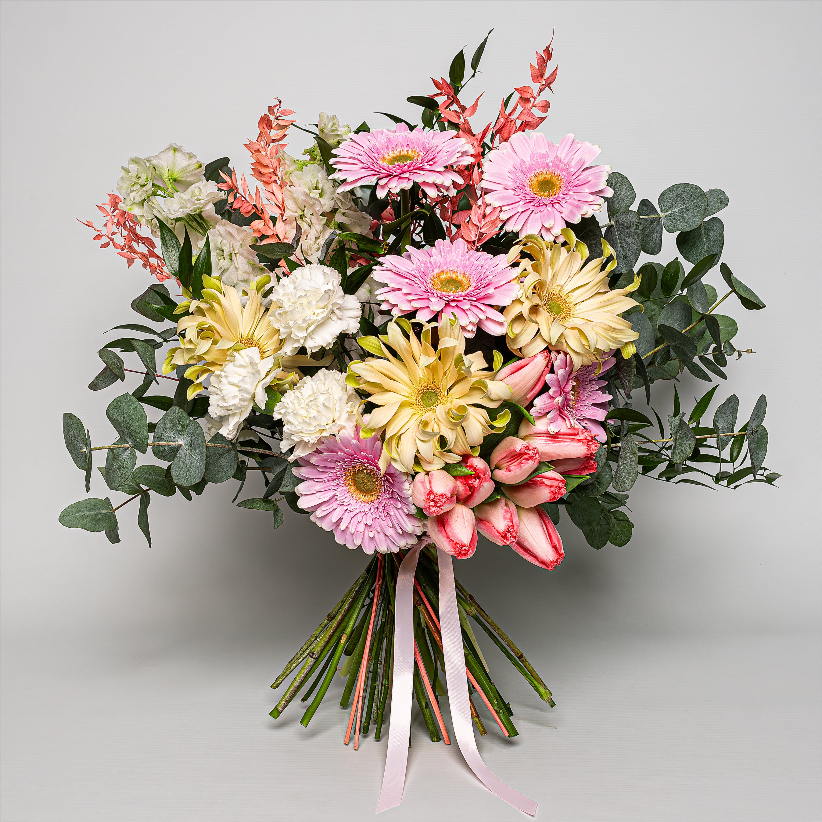 Florist Choice radiates with spring's soft, warm hues, a fitting tribute to celebrate special events and occasions featuring gerbera daisies in shades of pink and creamy yellow, their large, sunny blooms symbolizing cheerfulness and purity. The delicate pink of the daisies is complemented by the subtle blush of tulips, whose petals have a gentle, painterly streak of pink and white. White carnations and chrysanthemums offer a soft delicate look.