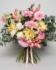 Florist Choice radiates with spring's soft, warm hues, a fitting tribute to celebrate special events and occasions featuring gerbera daisies in shades of pink and creamy yellow, their large, sunny blooms symbolizing cheerfulness and purity. The delicate pink of the daisies is complemented by the subtle blush of tulips, whose petals have a gentle, painterly streak of pink and white. White carnations and chrysanthemums offer a soft delicate look.