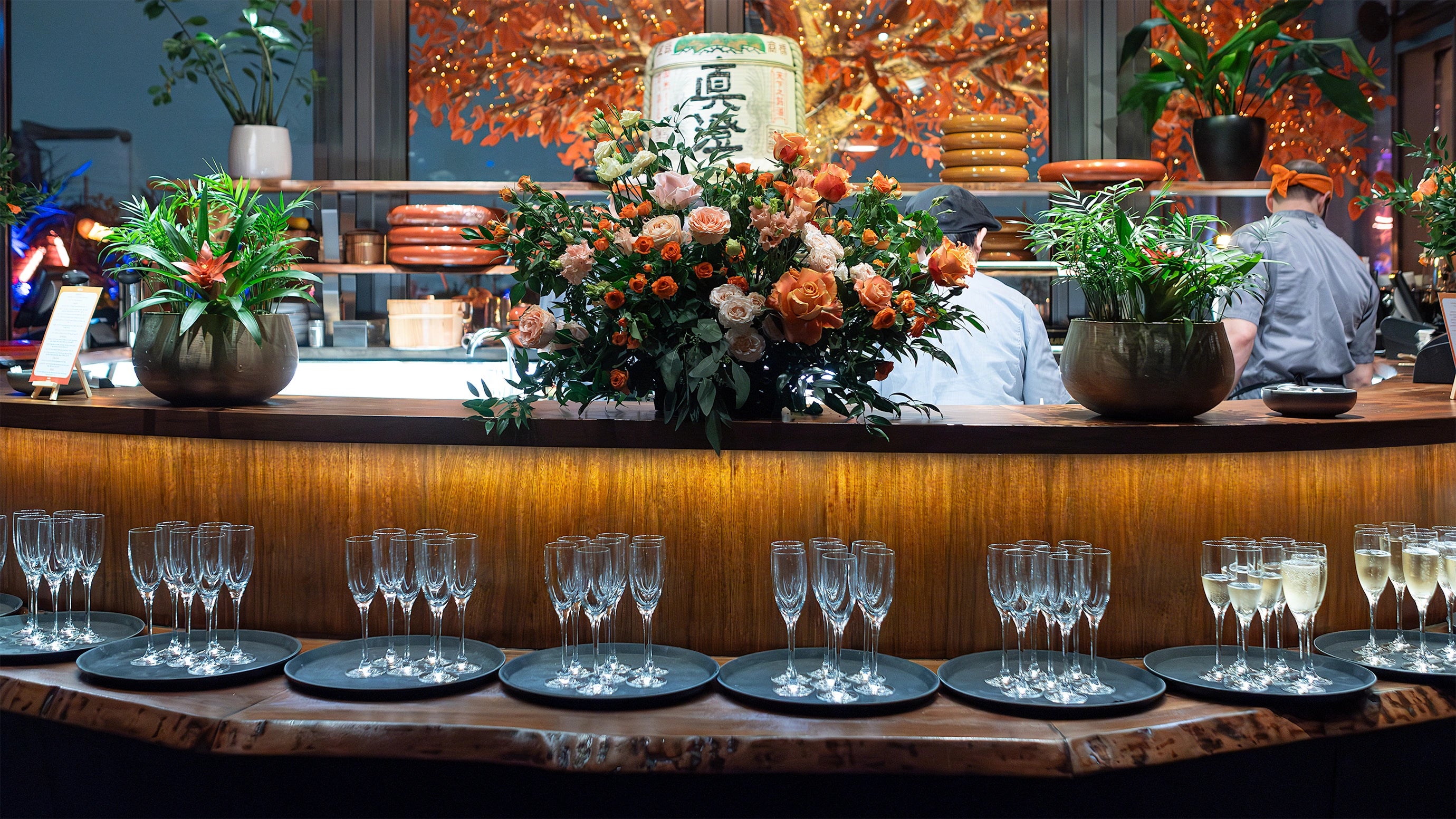 A close-up of a bespoke flower table arrangement with vibrant orange and soft cream roses in a textured glass vase in the luxurious setting of the EasyJet annual partner event in London - Amaranté London