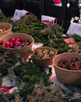 Close-up of Christmas wreath-making materials including pinecones, baubles, fresh greenery, and ribbons laid out for participants.