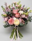 Spring Bloom Fresh Flower Bouquet is a luxury floral arrangement with several large, ruffled roses in varying shades of pink and peach, their opulent petals unfurling amidst the surrounding greenery. A delicate collection of blooms in soft pastel shades, suggesting sophistication and grace. It includes blushing pink roses, creamy white lisianthus, and hints of lavender and pale green, creating a harmonious visual symphony.
