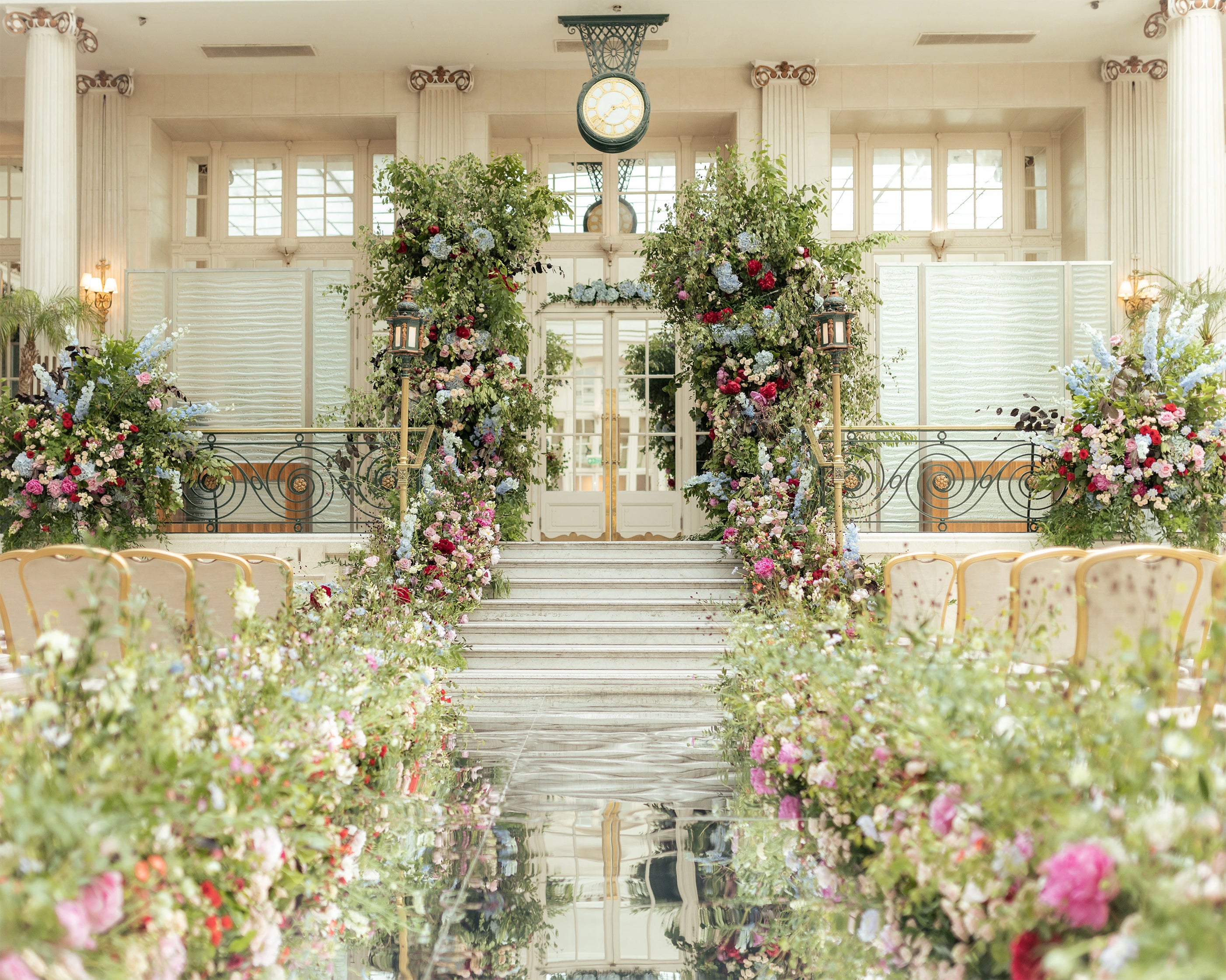 Wedding ceremony setup with floral arch and aisle in elegant venue with columns and natural lighting - Floral Design by Amaranté London