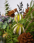 Decorative arrangement with green fruits, cinnamon sticks, and pine branches on a light gray background
