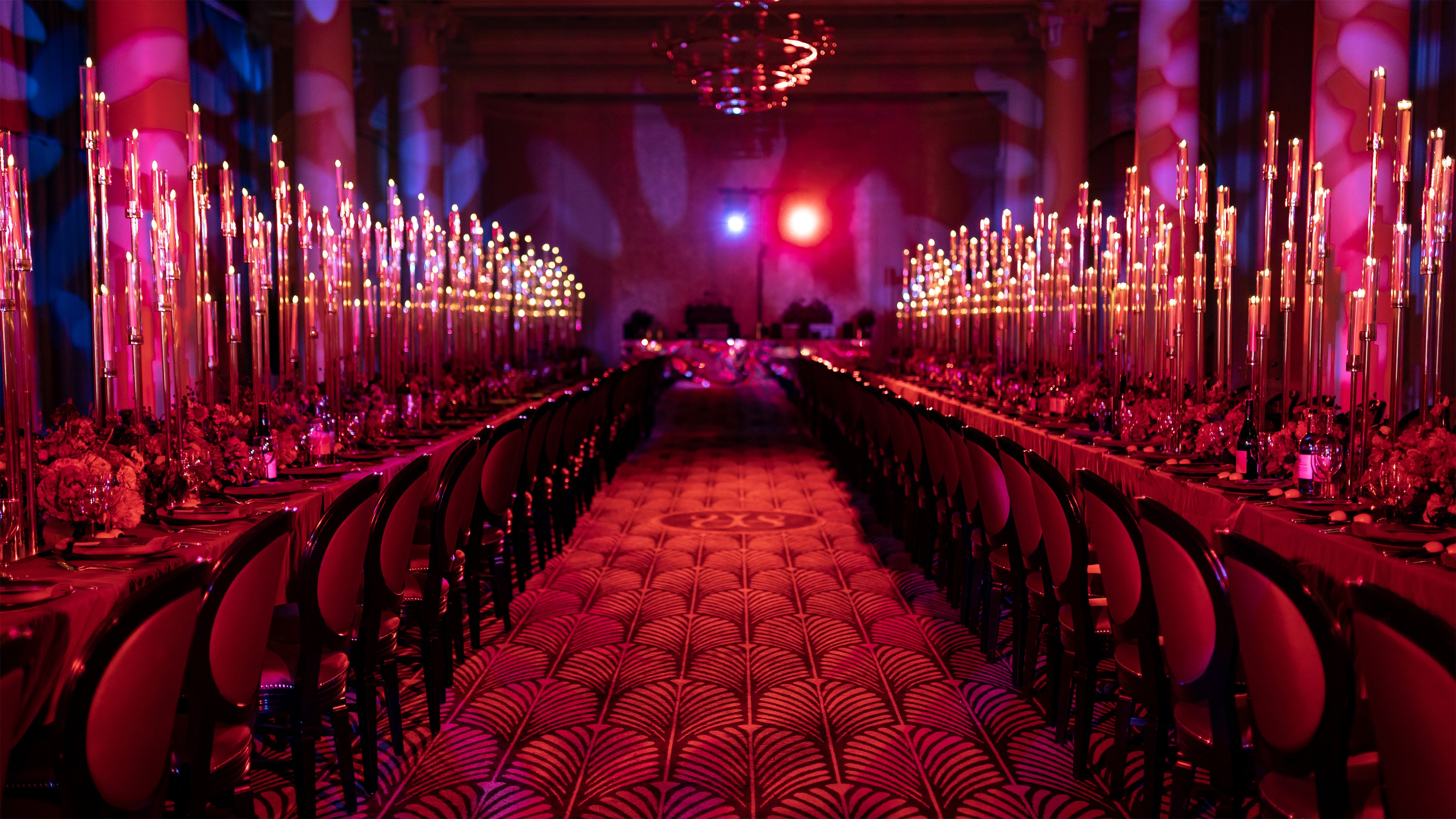 The Waldorf Hilton reception features tall taper candles, abundant red floral centerpieces on banquet tables, and atmospheric pink and red lighting, creating an opulent and romantic ambiance - Amaranté London.
