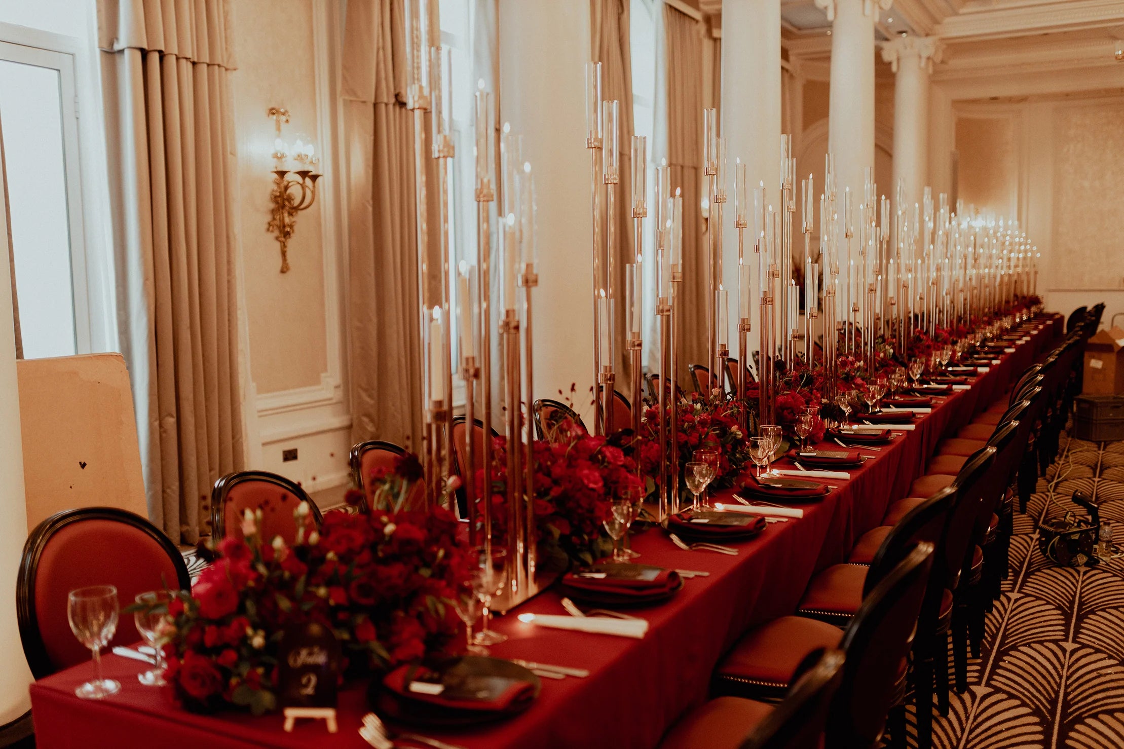 Opulent red floral centerpieces at Waldorf Hilton banquet with dramatic tall taper candles in gold holders creating a luxurious tablescape along an extended dining table - Amaranté London.