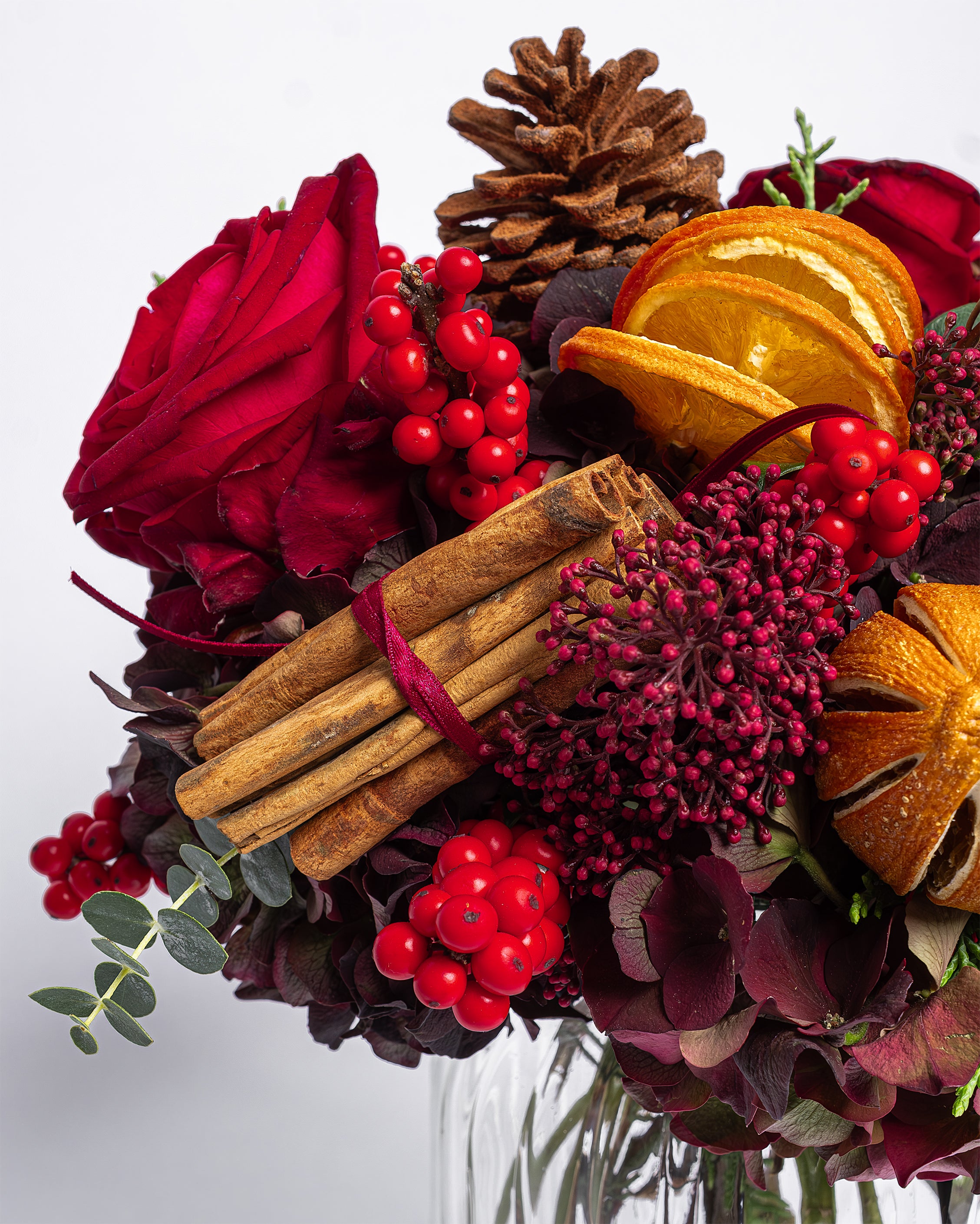 Decorative arrangement with red flowers, berries, cinnamon sticks, and oranges on a white background