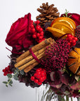 Decorative arrangement with red flowers, berries, cinnamon sticks, and oranges on a white background