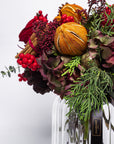 Bouquet of flowers with fruits and berries in a clear vase on a white background