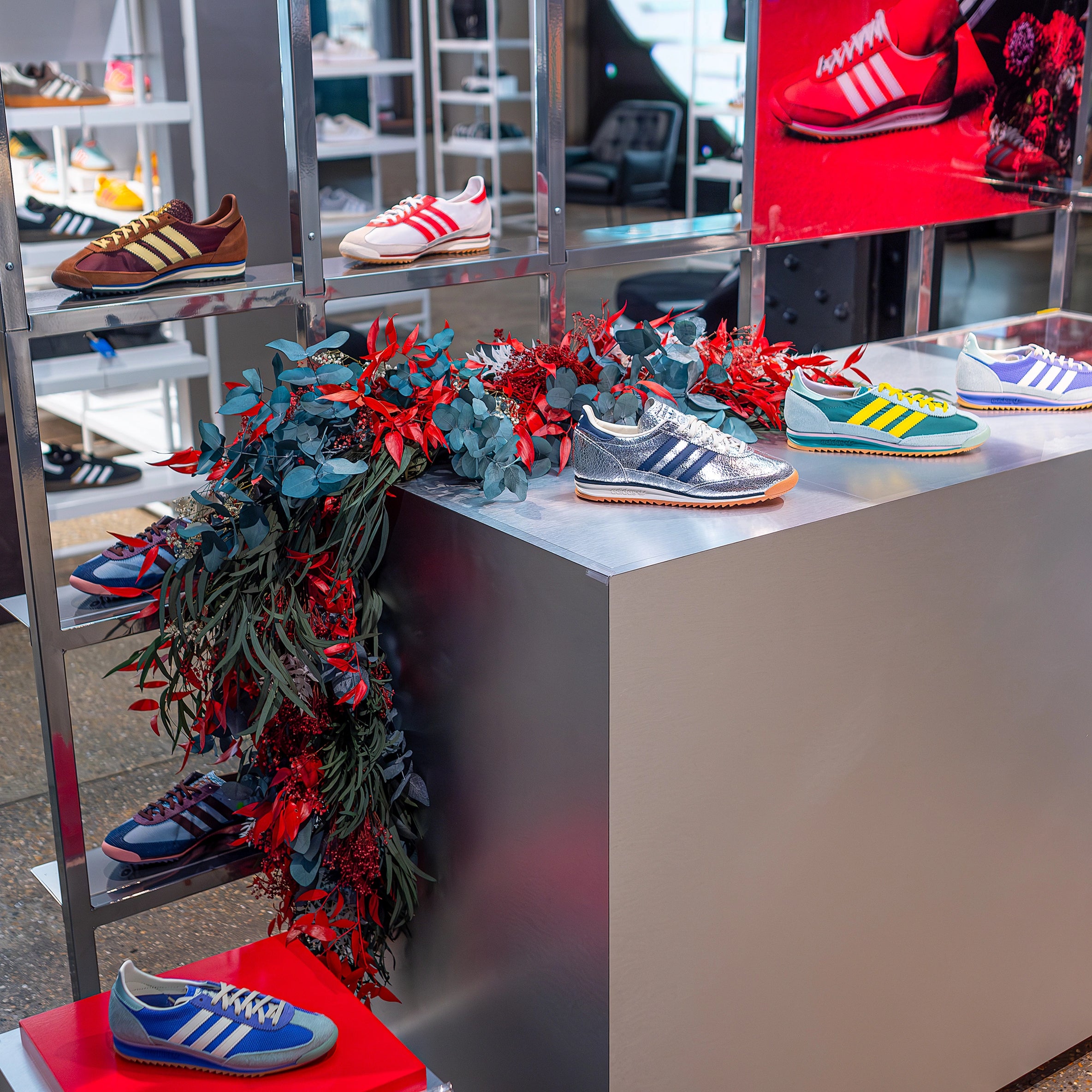 Close-up view of a floral garland installation by Amaranté London at Adidas Bond Street store. The installation combines red and green floral arrangements that complement the SL72 collection display to reflect the blend of luxury and sportiness Adidas aims to portray.