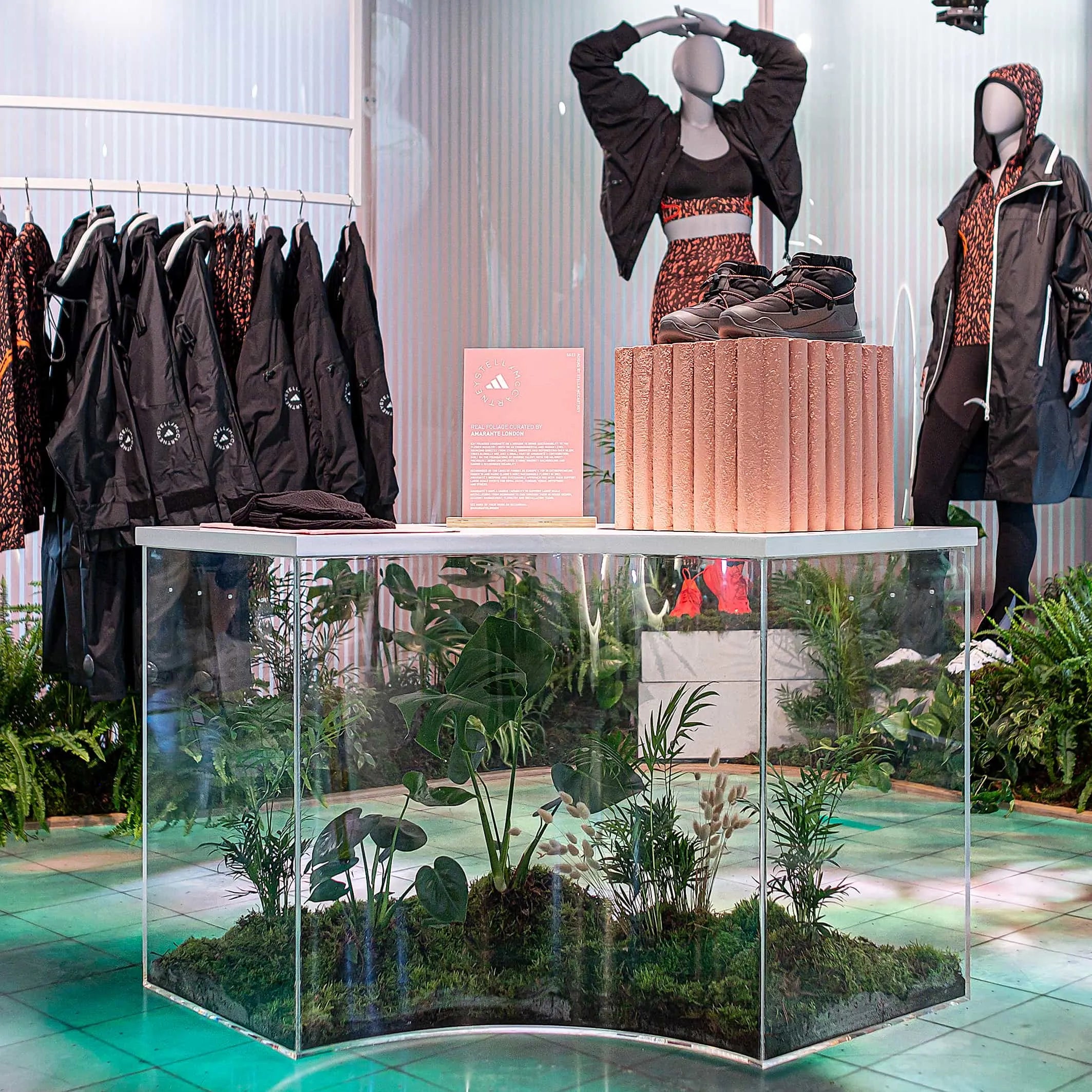 An elegant display at Adidas x Stella McCartney's aSMC launch was designed by Amaranté London, featuring athletic footwear atop a clear case of vibrant greenery, reflecting the event’s dedication to combining high fashion with natural aesthetics.