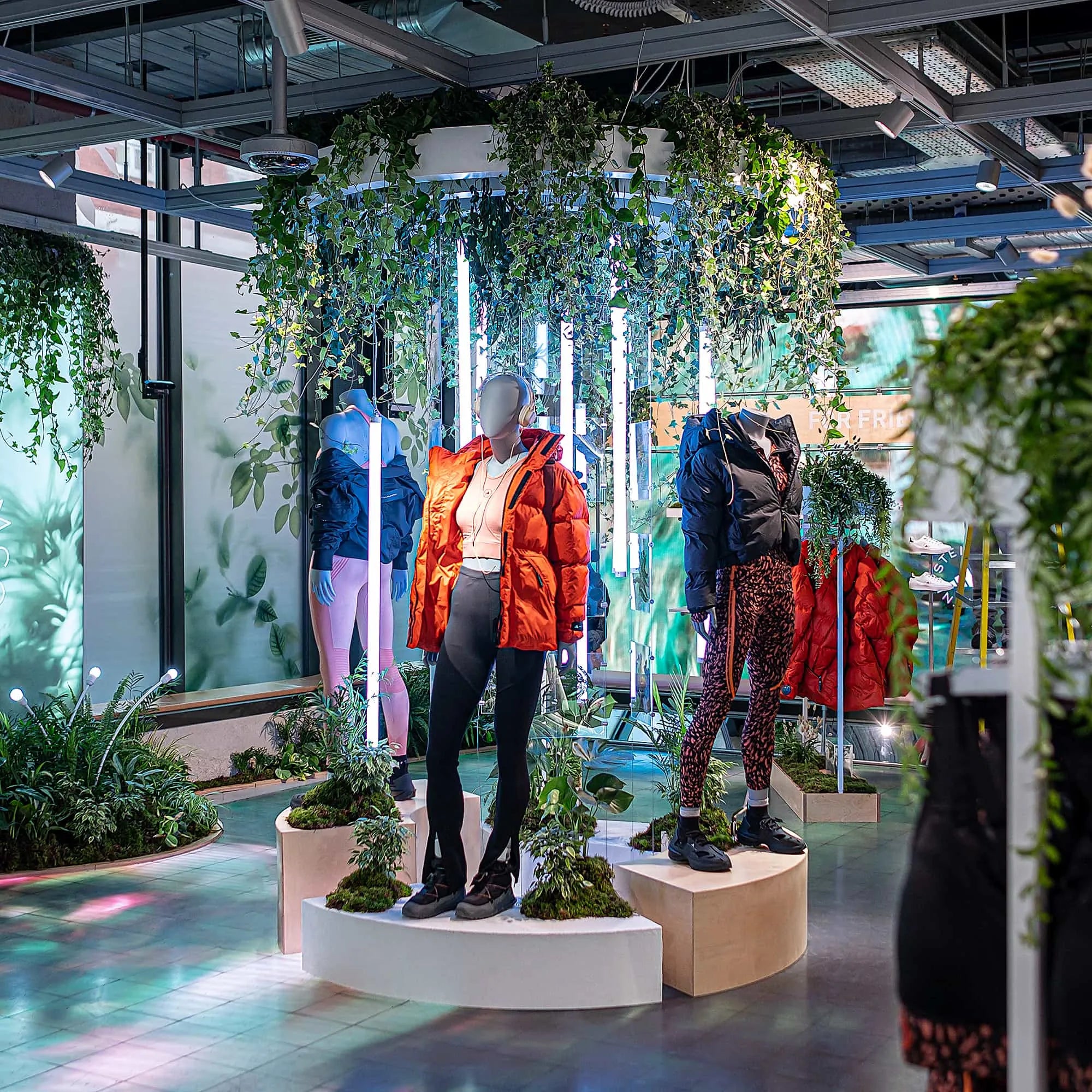 Mannequins dressed in Adidas x Stella McCartney aSMC collection are arrayed on pedestals amidst a lavish display of greenery by Amaranté London Event Florist, offers a harmonious blend of bold sportswear and delicate foliage, emblematic of sustainable luxury fashion.