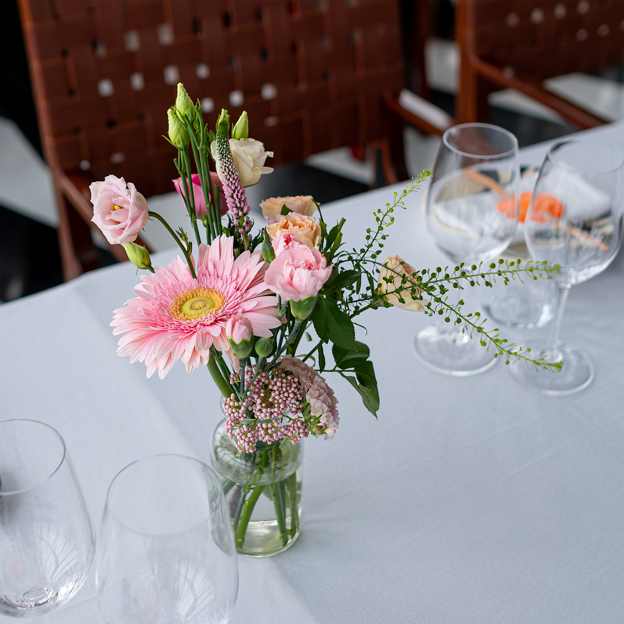 Close-up of luxury bud vase arrangement by Event Florist Amaranté London at the Chanel event in SUSHISAMBA. The arrangement features a pink gerbera daisy and pastel roses in a clear glass vase, adding a touch of spring to the elegant table setting.