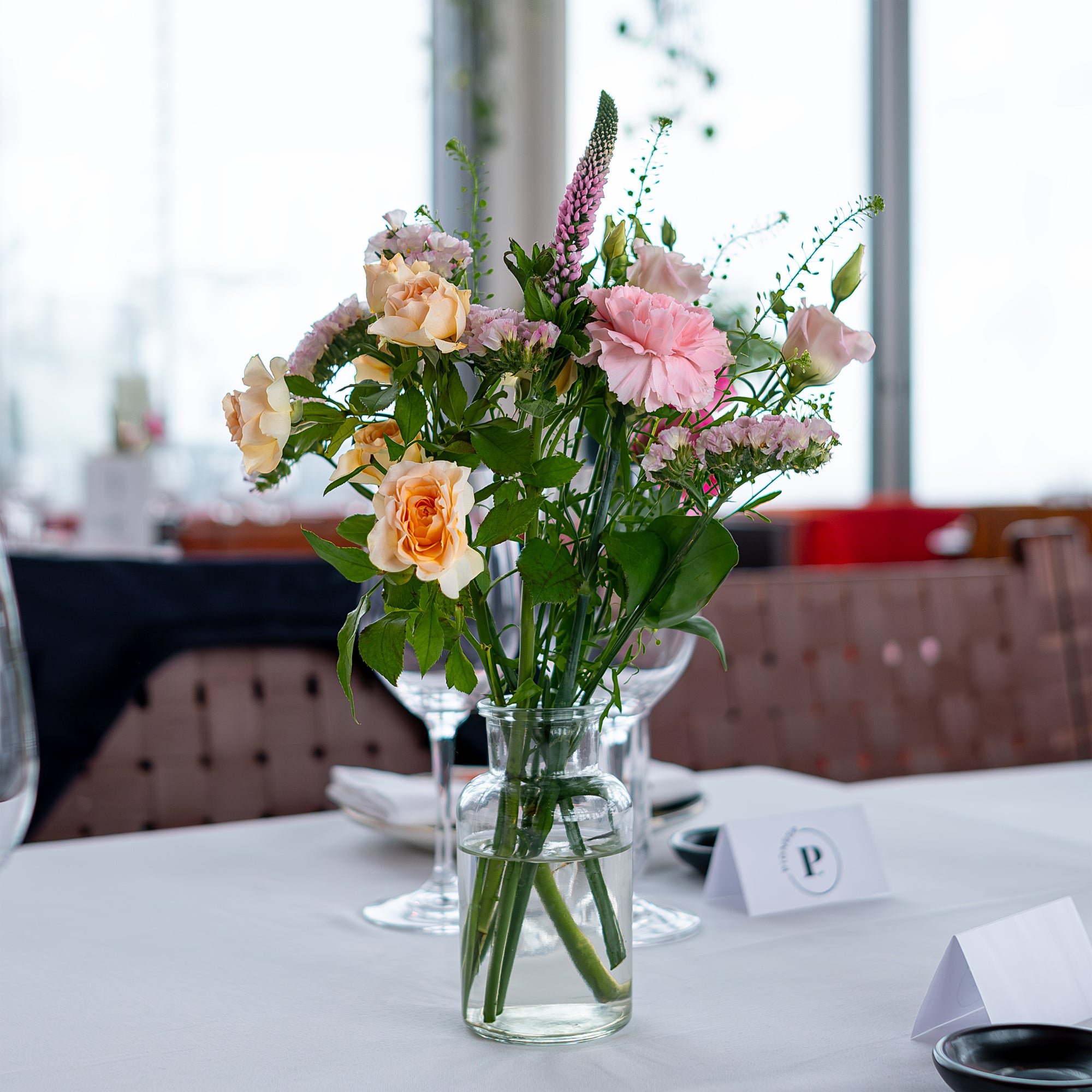 A luxury table floral arrangement featuring a single large peach rose surrounded by greenery and purple accents, designed by event florist Amaranté London for the Chanel event in SUSHISAMBA. Sophisticated floral decor that enhances the luxurious dining experience.