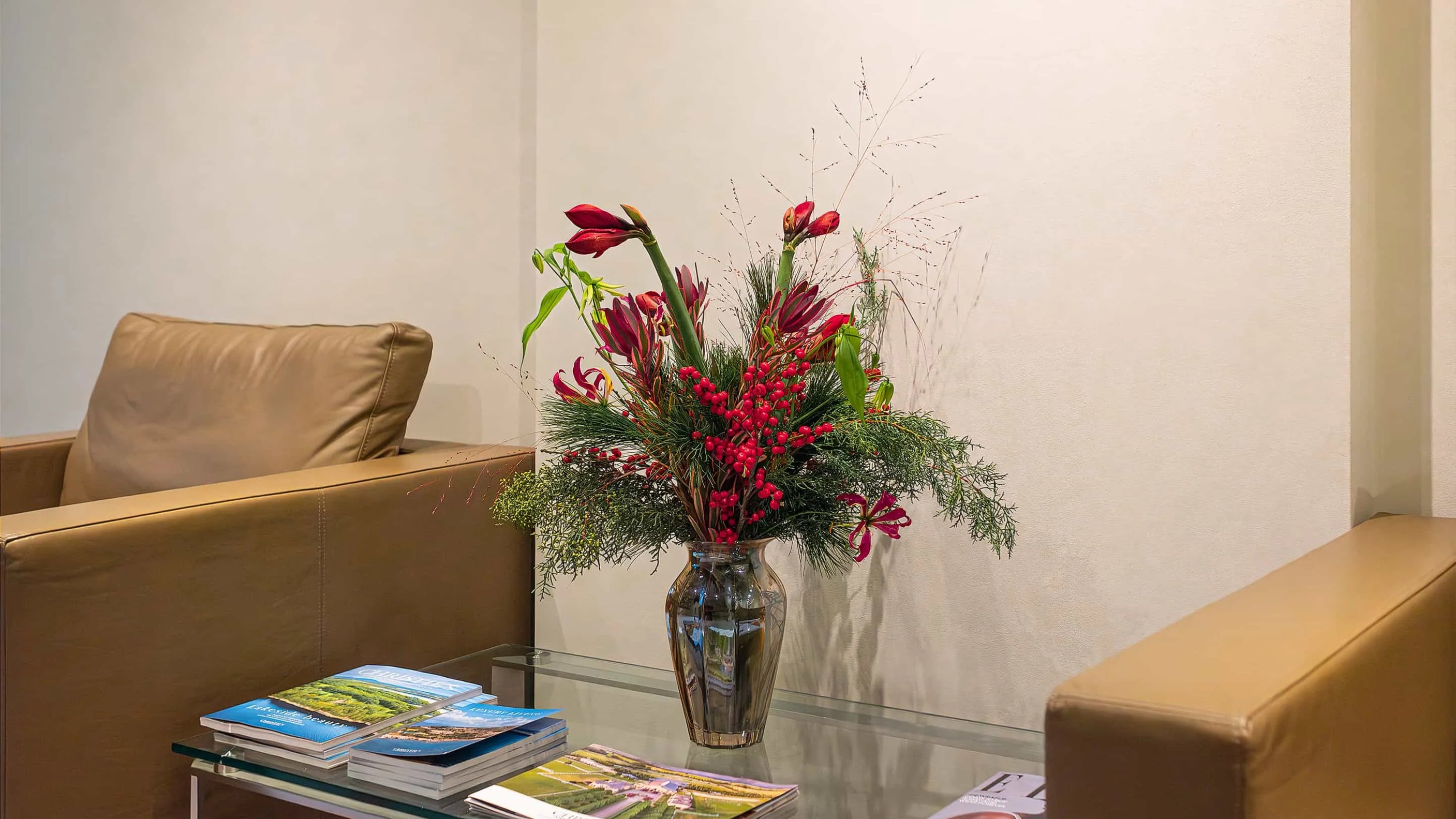 Christmas Bouquet on a coffee table at Christie's - an elegant floral arrangement featuring striking red Alstroemeria flowers and vibrant Ilex berries, complemented by delicate greenery and set in a sleek transparent glass vase, designed, created and installed by Event Florist Amaranté London