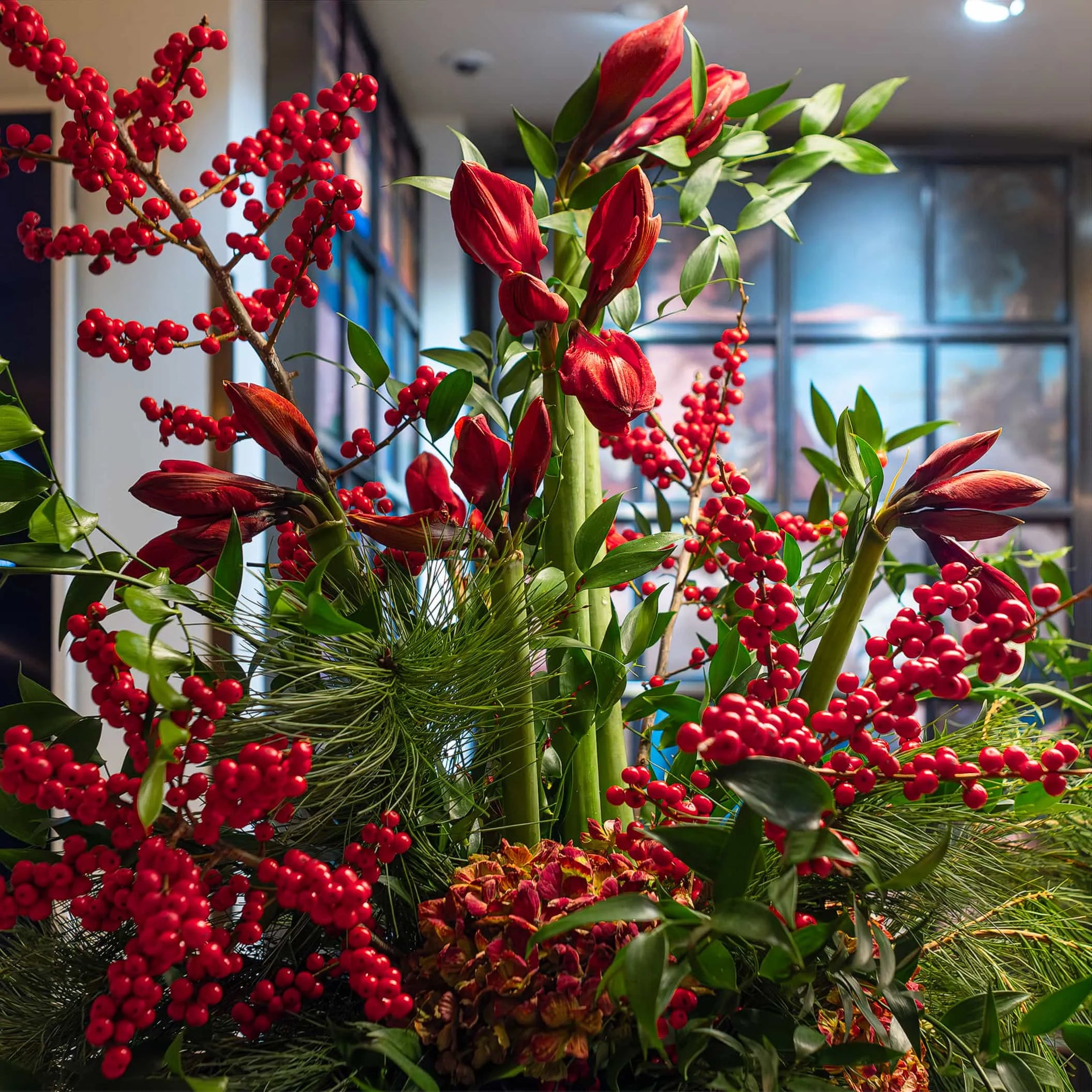 Closeup view of Christmas flowers in the regal purple vase with deep reds and bright greens at Christie's by Amaranté London