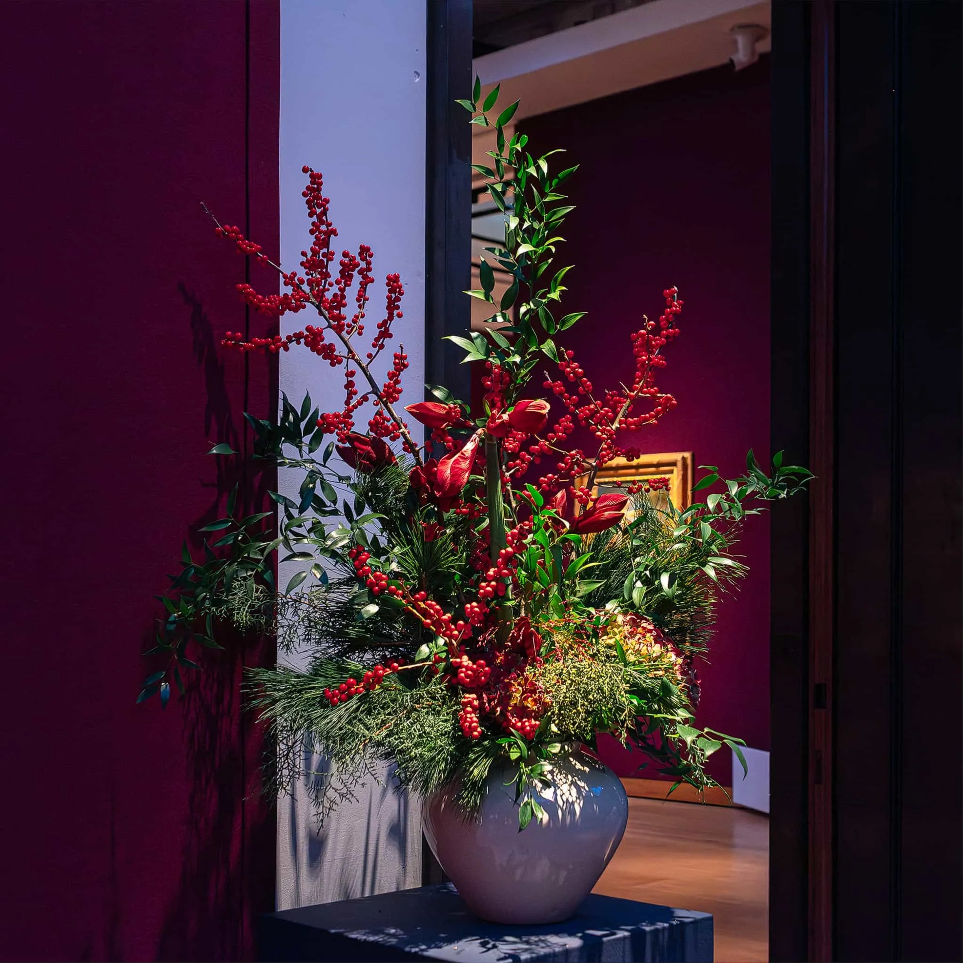 A regal purple vase cradles a festive bouquet with deep reds and bright greens for a luxurious bespoke Christmas bouquet at Christie's by Amaranté London