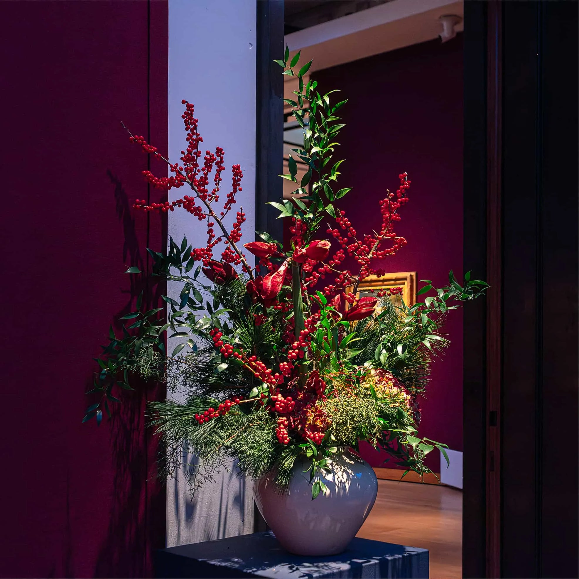 A regal purple vase cradles a bouquet of Christmas Flowers in deep reds and bright greens at Christie's, designed, created, and installed by event florist Amaranté London.