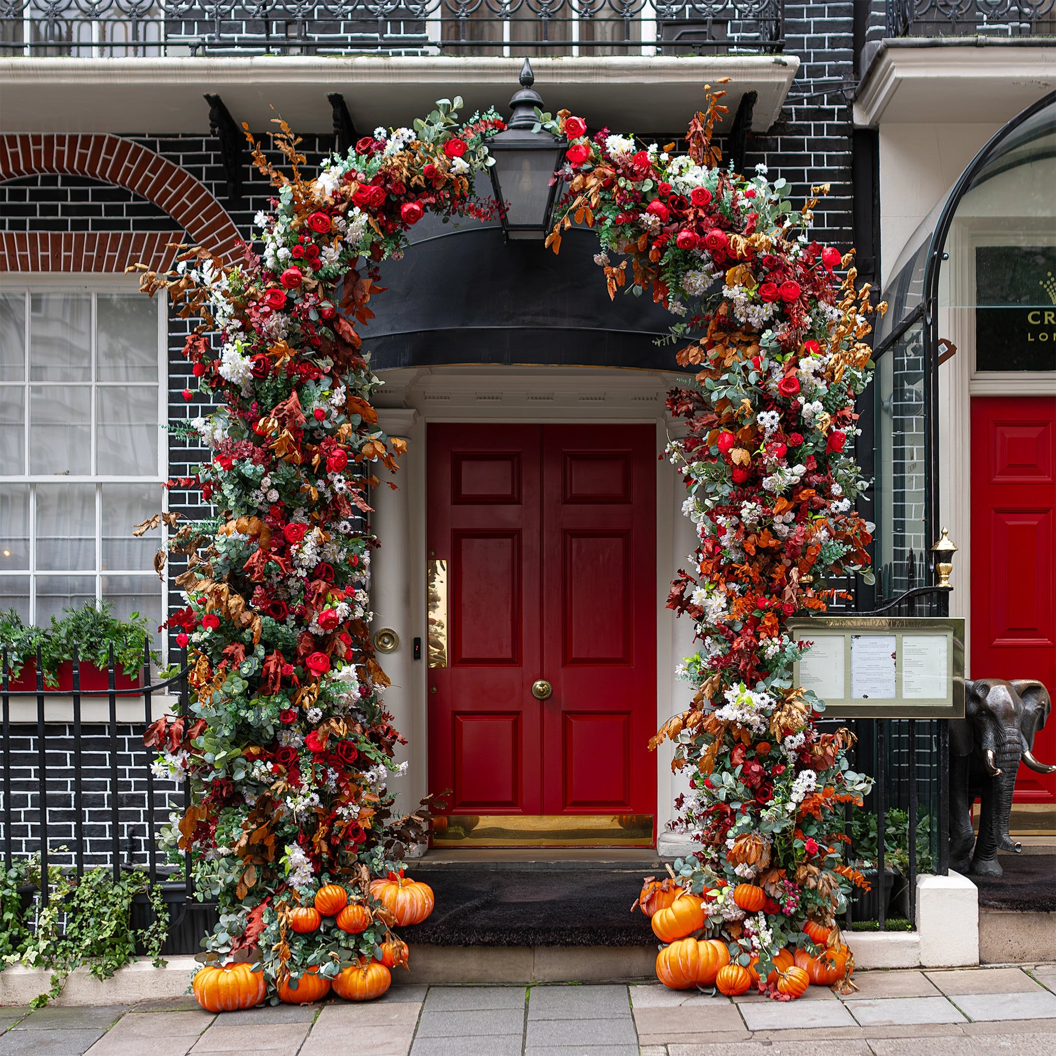 A closer view of the elegant floral archway installation by Event Florist Amaranté London at Crown London. The image highlights the plentiful red roses, lush greenery, and autumnal hues, enhancing the luxurious ambience of the venue entrance.