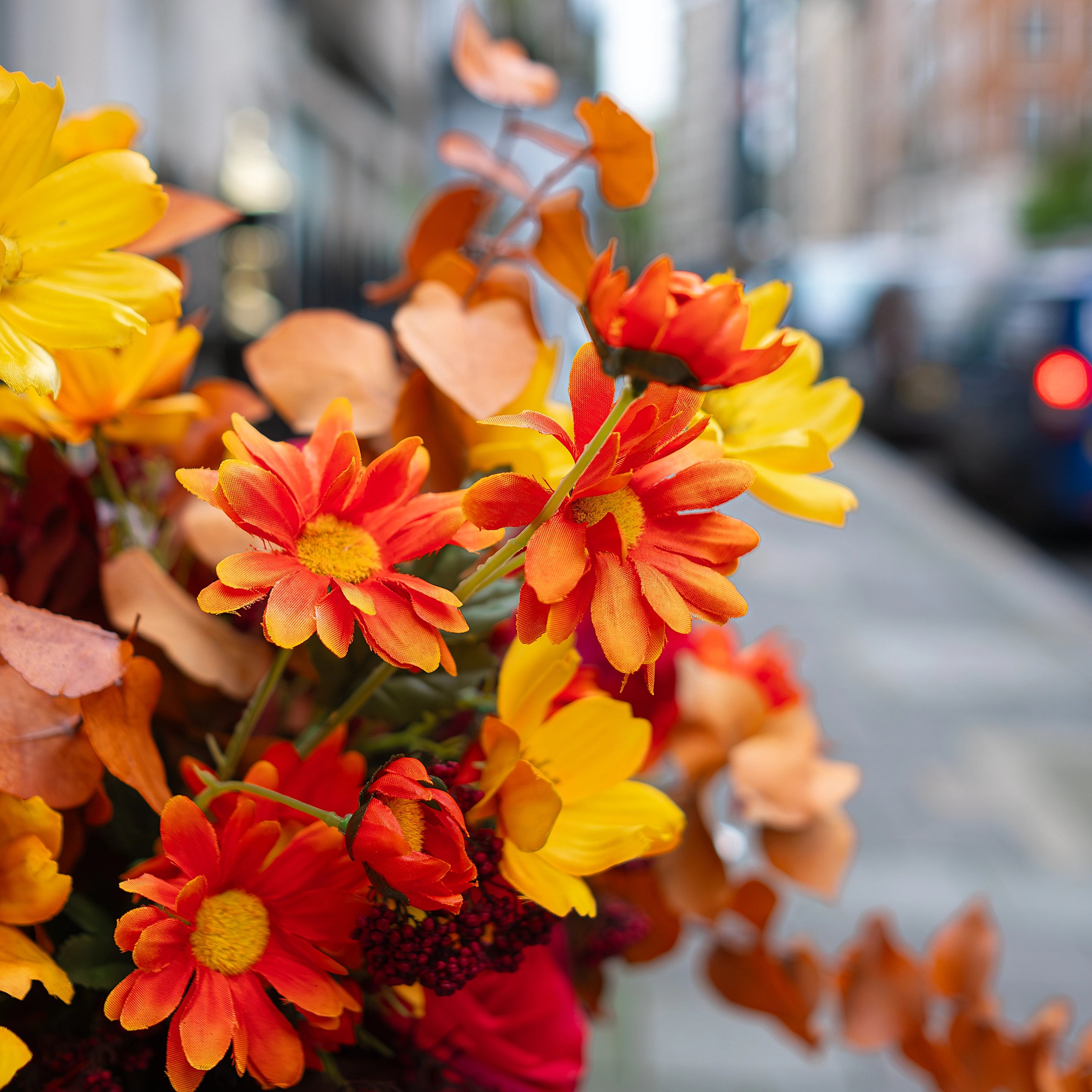Detailed close-up of a floral basket arrangement for Crown London. The basket is filled with yellow daisies, rich red roses, and warm orange blooms framed by autumnal foliage. The floral design aimed at creating a seasonal arrangement to add a joyful, vibrant accent to the entrance while blending effortlessly with the upscale decor of the members club entrance.