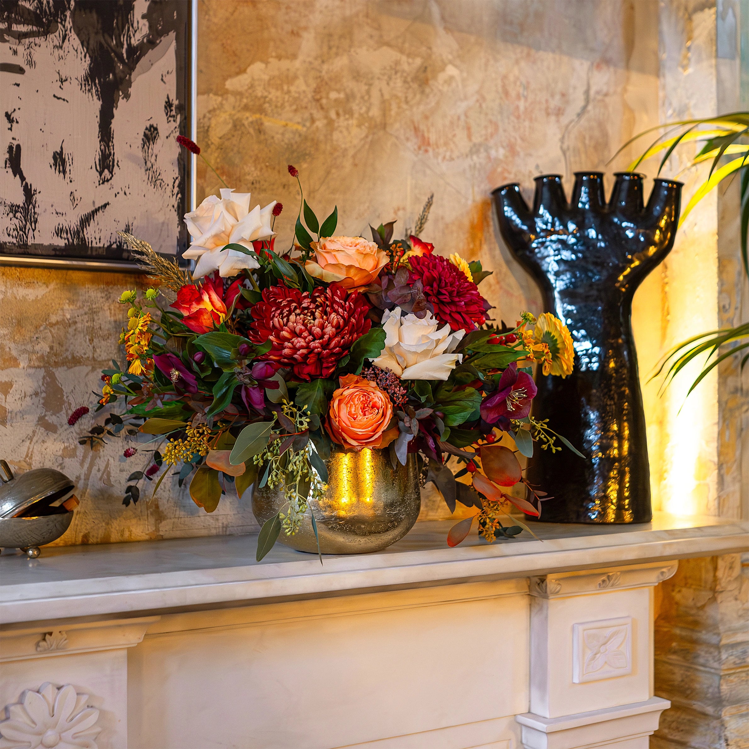 Bespoke autumn floral arrangement featuring red chrysanthemums, garden roses and seasonal foliage styled on a marble mantelpiece, private residence flower service London by Amarante London