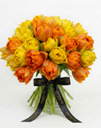 Luxurious bouquet of golden and orange tulips arranged in rounded dome shape, tied with elegant black Amarante London ribbon against white background - Amaranté London