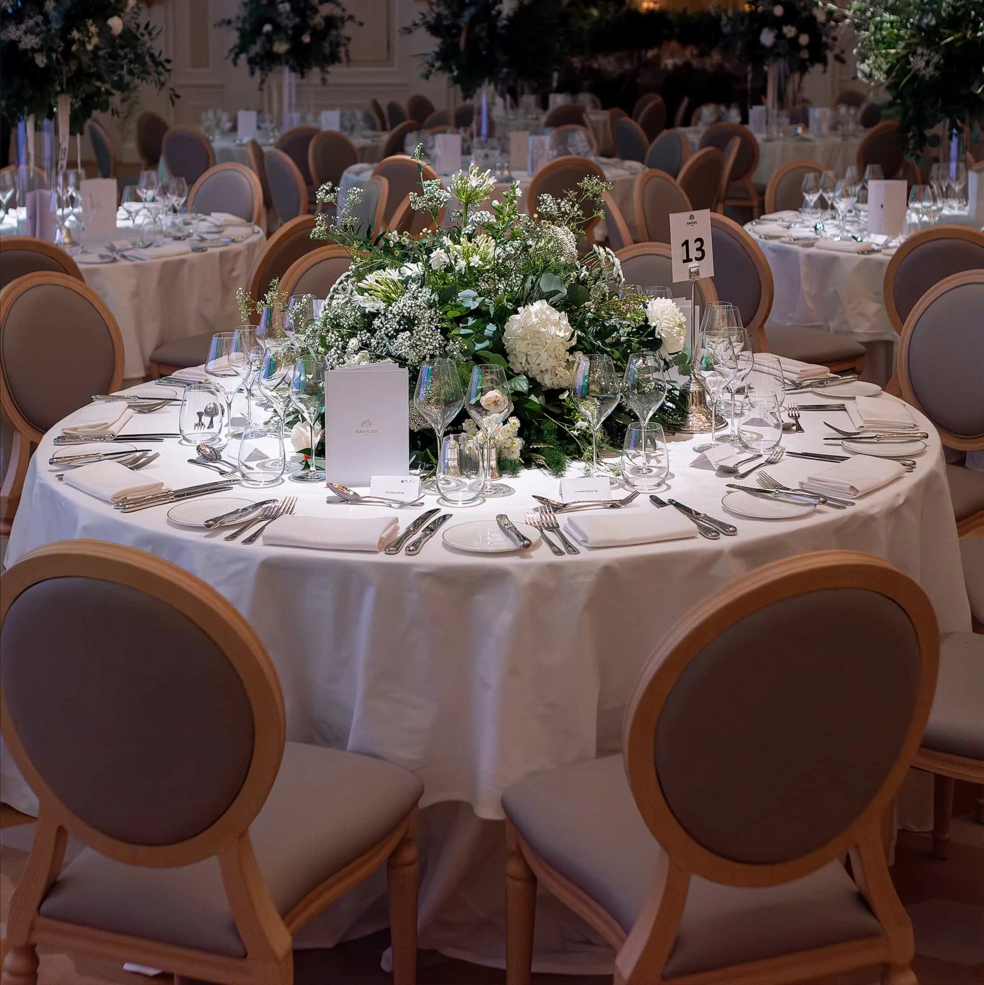 In this image, a round table was elegantly prepared for the FTI Consulting corporate event, using pristine white linens, fine cutlery, and crystal glassware. The table was crowned with a lush, handcrafted floral centrepiece designed and made by Amaranté London, an Event Florist in London.