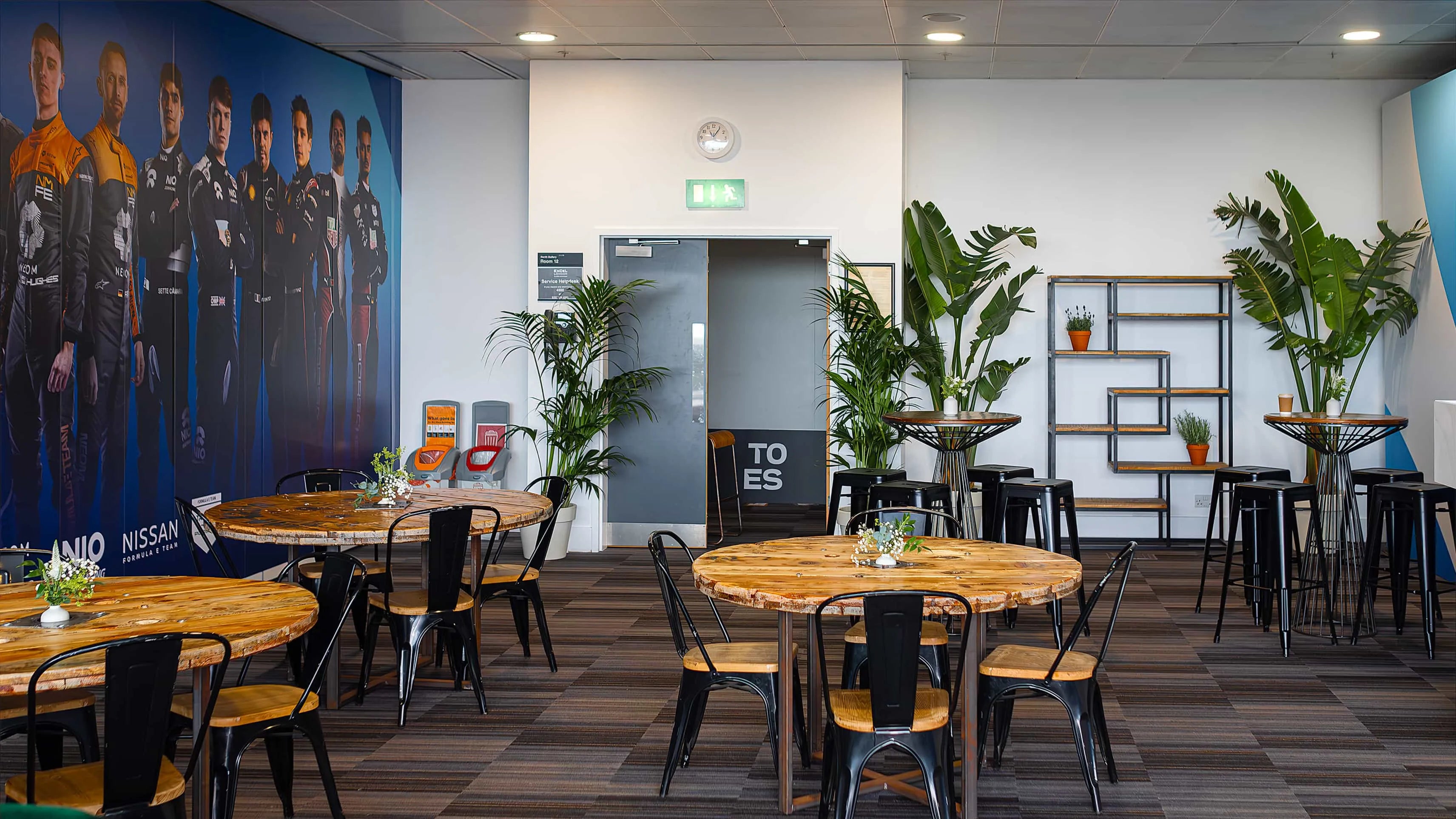 A spacious and well-appointed event dining area features rustic wooden tables with small, delicate floral arrangements and large potted plants, creating a natural and inviting atmosphere for Formula E guests in London - Amaranté London.