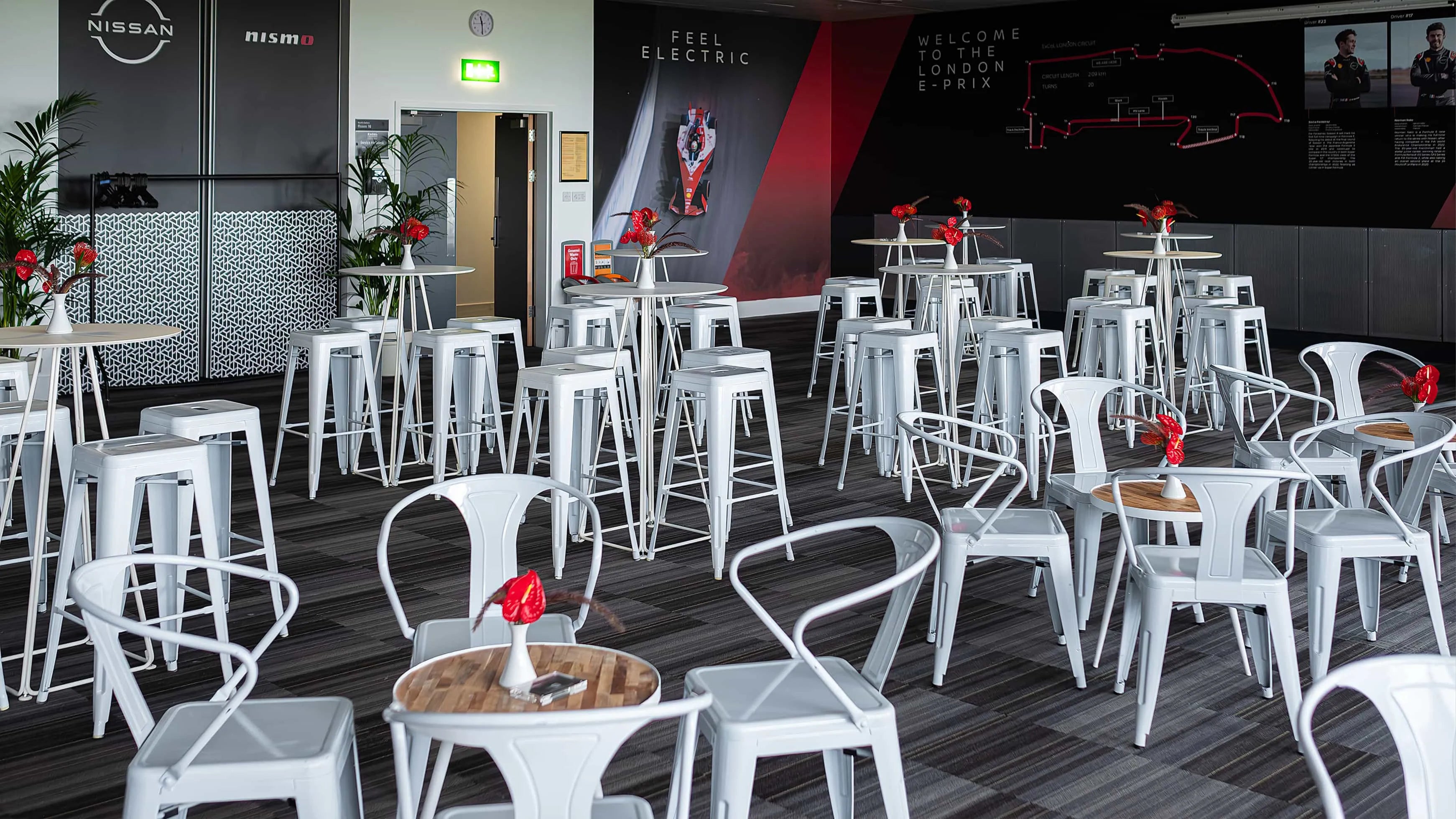 A Modern event space at the Formula E event in London, adorned with stylish white furniture and striking red anthurium centrepieces, creates a lively and welcoming environment for guests - Amaranté London.