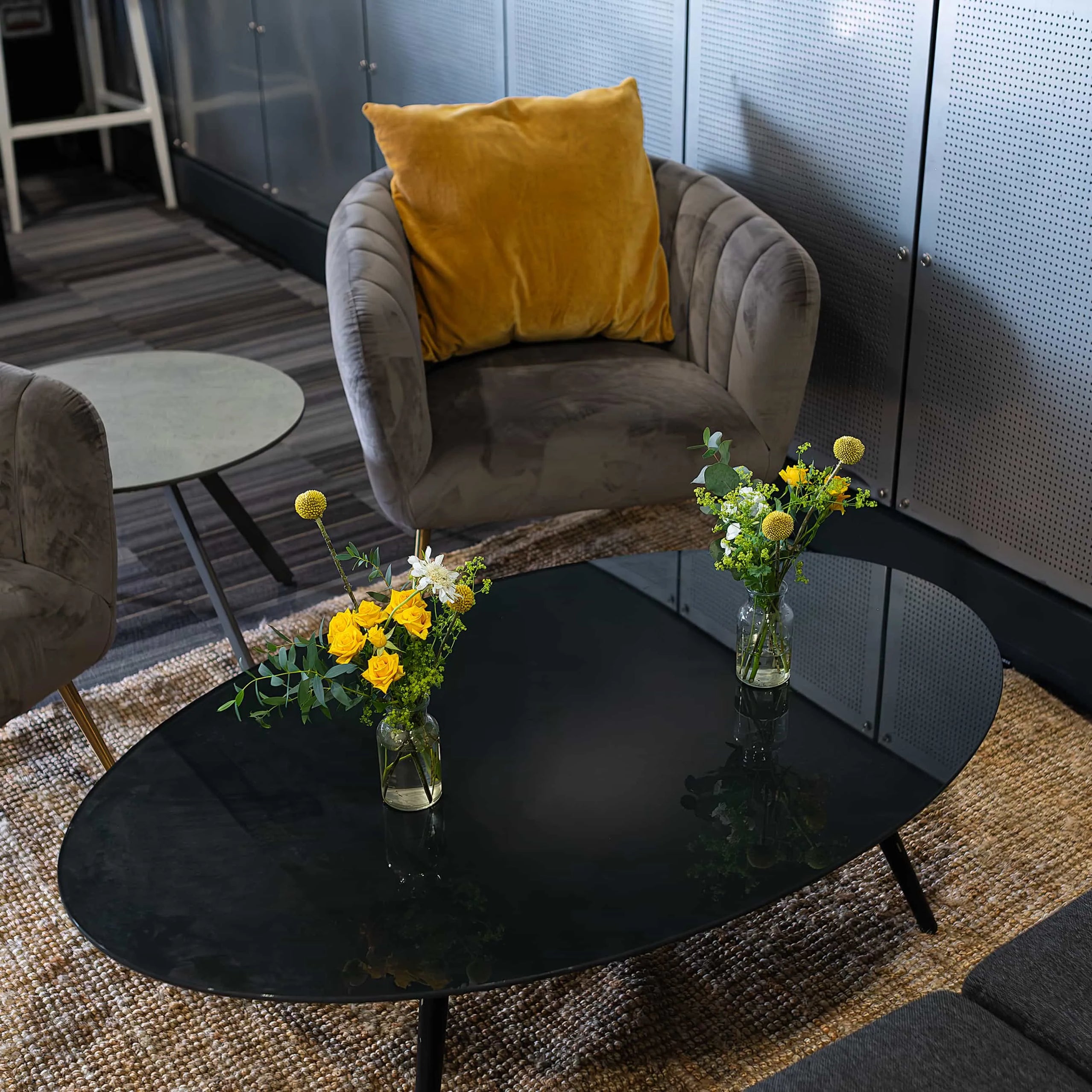 Elegant comfort in the lounge area at the Formula E Championship featuring subtle floral touches with yellow and white flowers in slim vases on a glossy black table, offering a sophisticated and calm setting - Amaranté London.