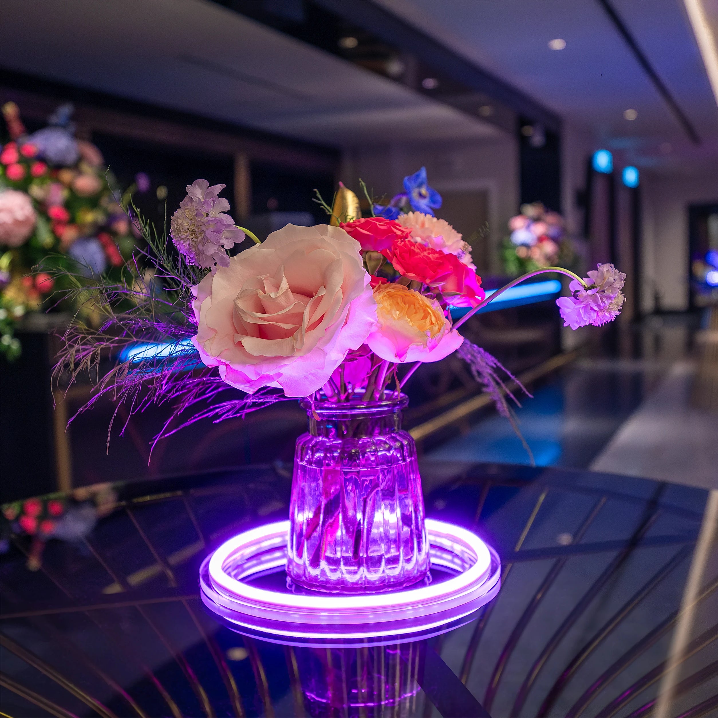 Small, vibrant floral arrangement on a purple light-up base, showcasing pink and yellow roses with delicate purple flowers, enhancing the modern ambiance at the Formula E Gala Dinner Event - Amaranté London.