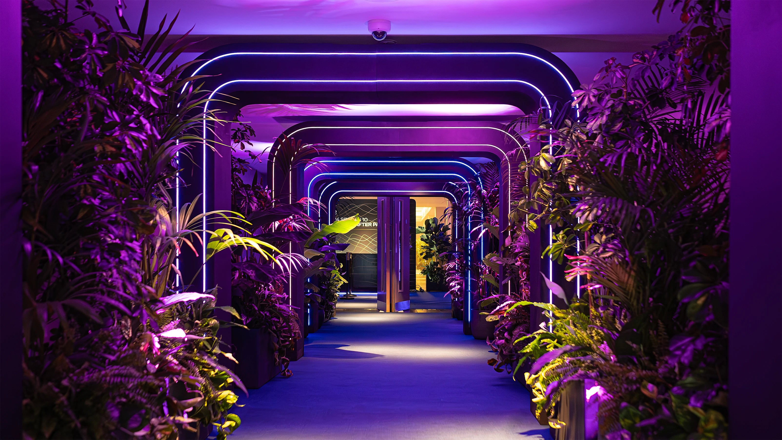 Futuristic hallway adorned with rows of lush greenery and neon lights, creating a striking contrast and immersive pathway. Floral arrangements designed, created and installed by Amaranté London for the Formula E Gala Dinner Event.