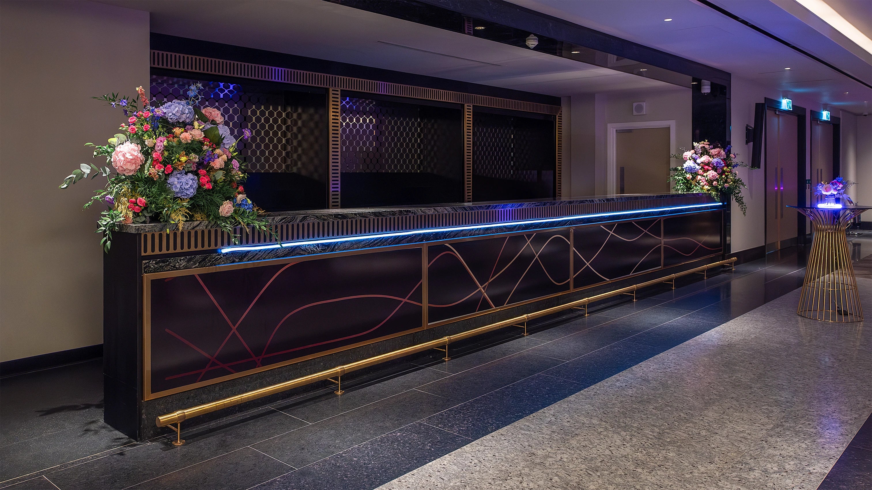 Elegant flower arrangements sitting on a sleek black counter, featuring roses, hydrangeas, and complementary foliage, all bathed in soft blue light - Bespoke contemporary floral artistry for events by Amaranté London.