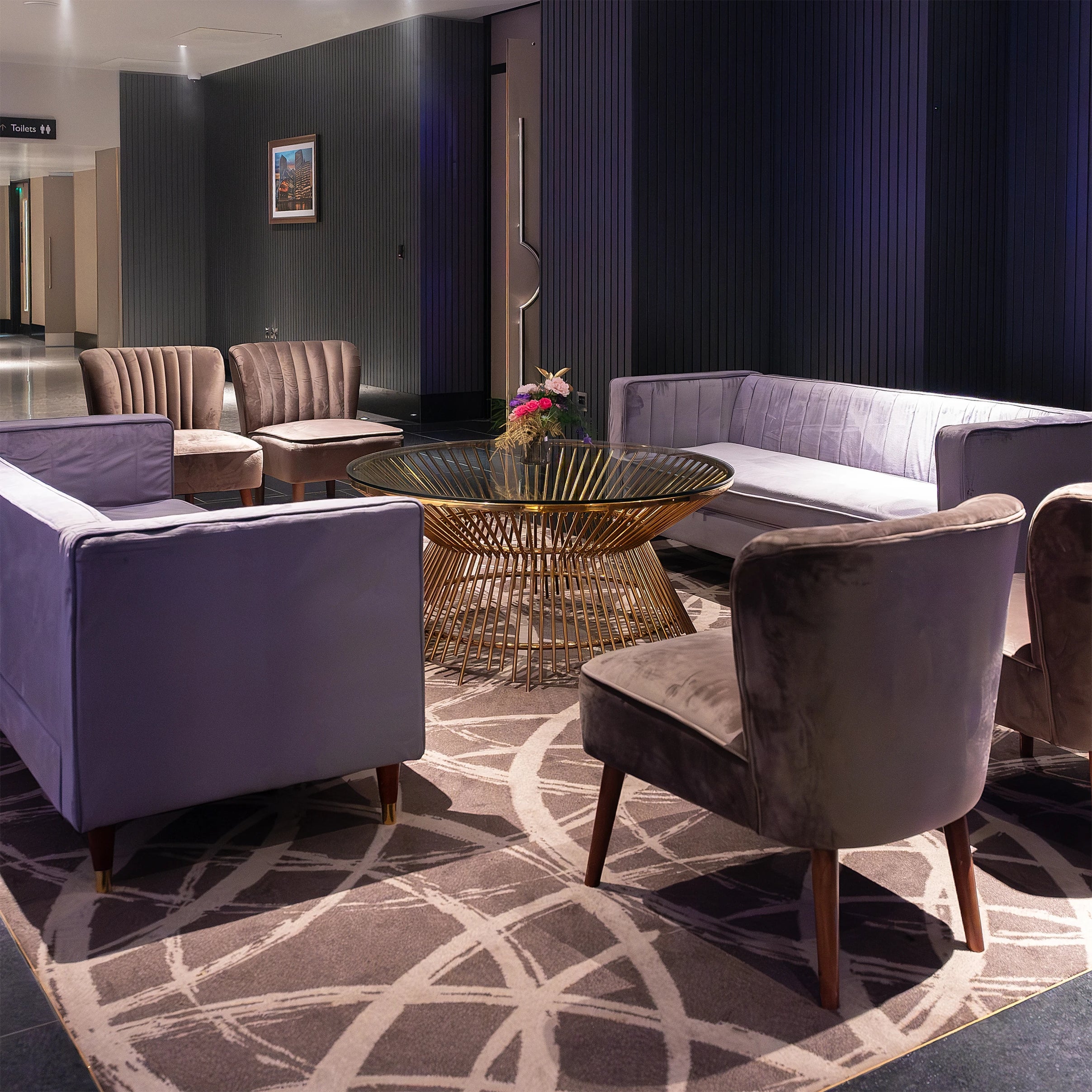 The elegant lounge setting at the Formula E Gala Dinner Event in London features plush purple velvet seating and a central gold wire coffee table accented by small, vibrant floral arrangements designed, created and installed by Event Florist Amaranté London to enhance the modern and luxurious atmosphere of the venue.