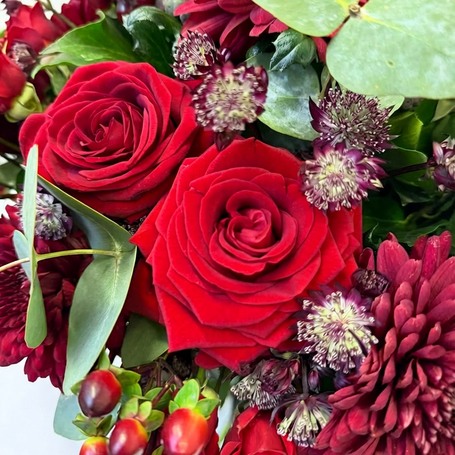 Close-up detail of premium red roses and burgundy astrantia flowers with eucalyptus leaves, showcasing the exquisite craftsmanship of luxury floral arrangement - Amaranté London