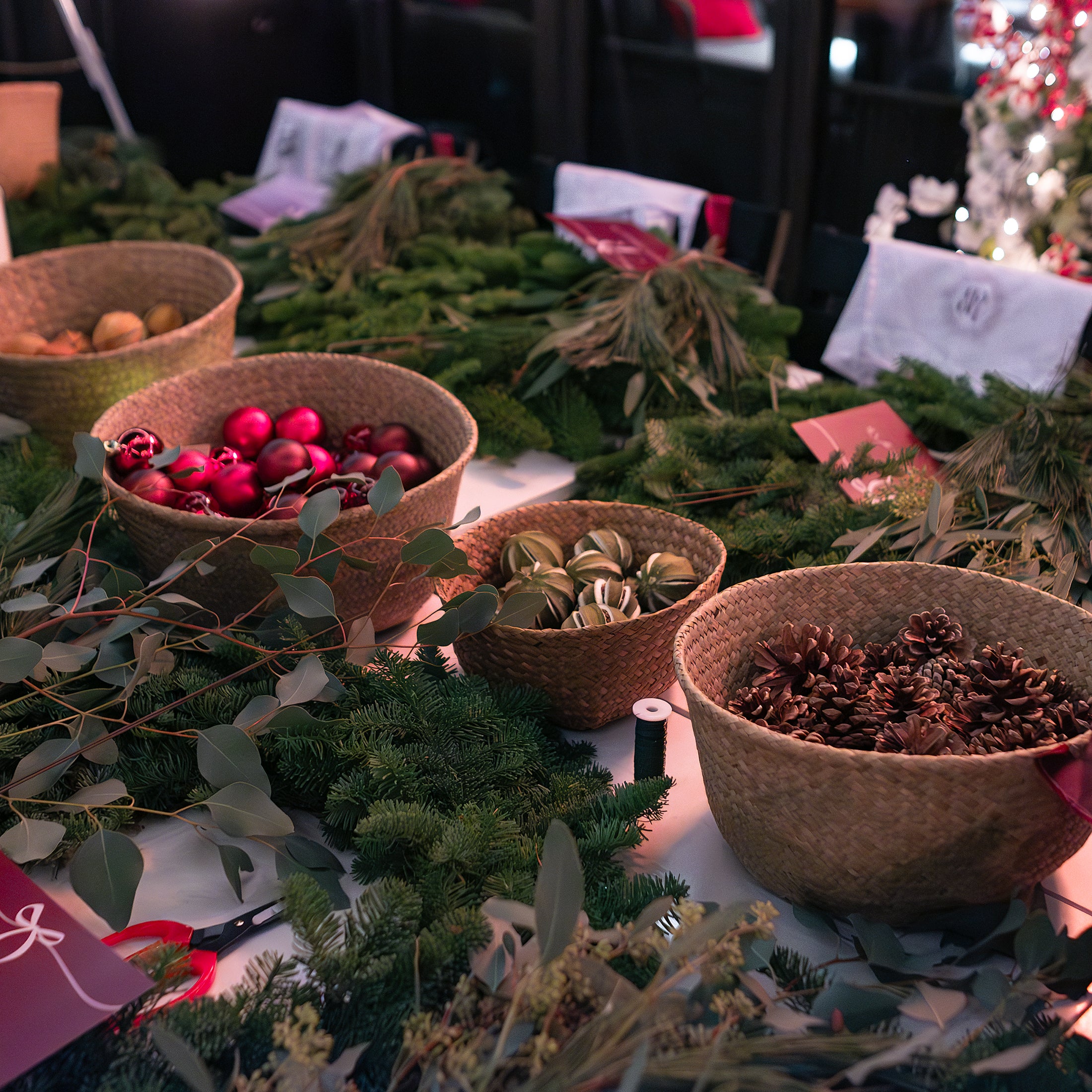 Close-up of Christmas wreath-making materials including pinecones, baubles, fresh greenery, and ribbons laid out for participants.