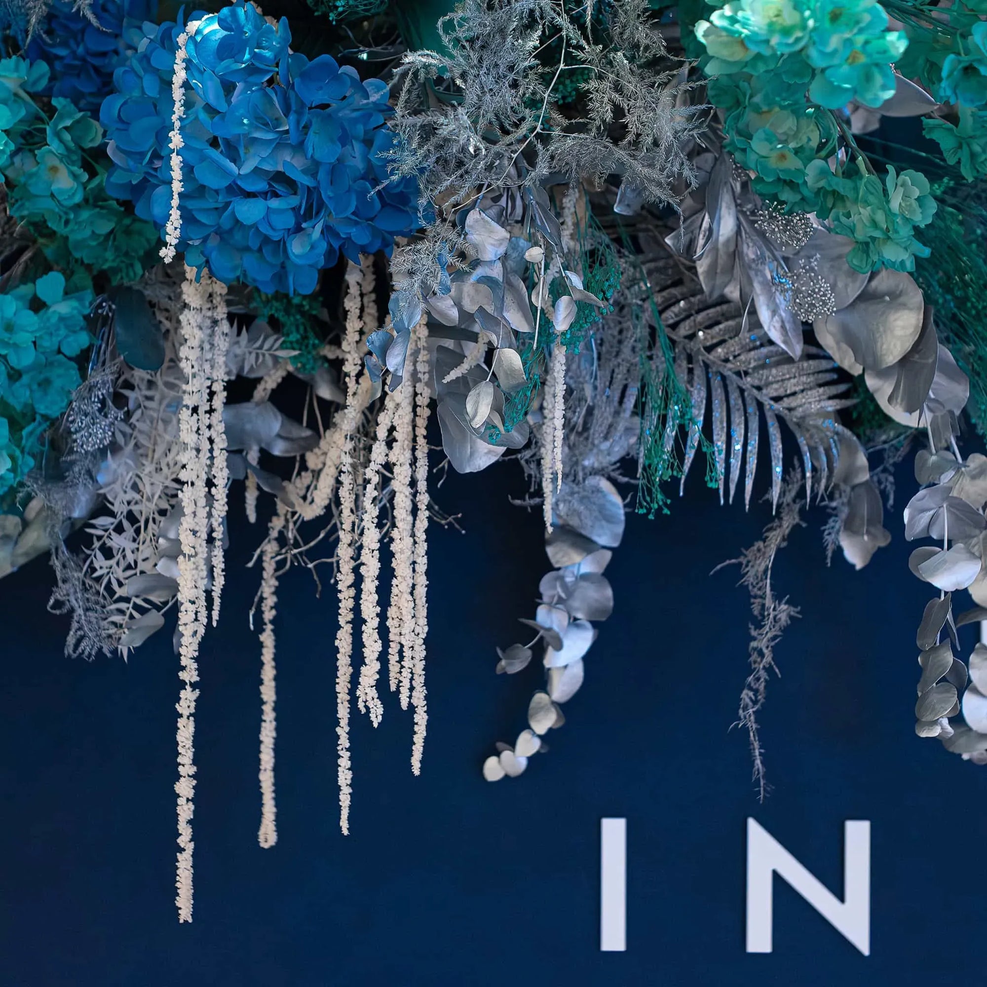Detailed image of Christmas Flowers for the IN MODE event at NOBU Hotel in London, featuring a variety of textures, including vibrant blue blooms, frosted greenery, silver-tinted leaves, and cascading white flowers.