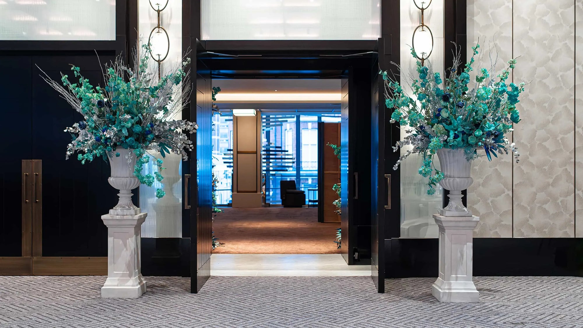 The grand entrance display at the InMode Christmas event at Nobu Hotel, designed by Event Florist Amaranté London, showcases large vases filled with teal and silver floral arrangements, adding a touch of elegance and festivity to the corporate event.