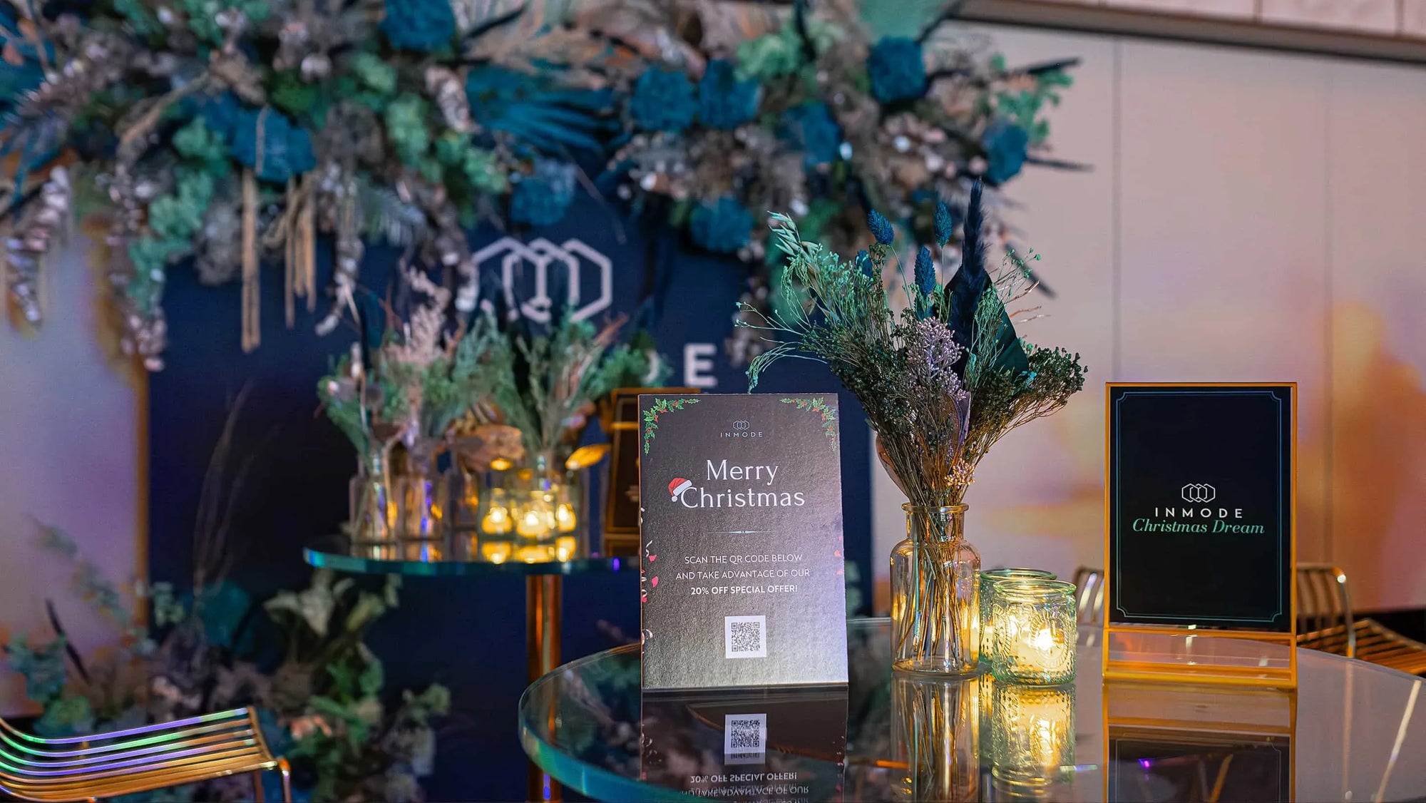 An image of the Christmas floral arrangement for a table at the InMode event at Nobu Hotel, designed by Event Florist Amaranté London, featuring a Merry Christmas sign, teal and silver floral centrepieces, and warm candlelight, creating a festive and elegant ambience.