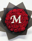 Elegant personalised red rose bouquet with white gypsophila letter 'M' centrepiece, wrapped in sophisticated charcoal paper against neutral background, luxury bespoke floral arrangement - Amarante London