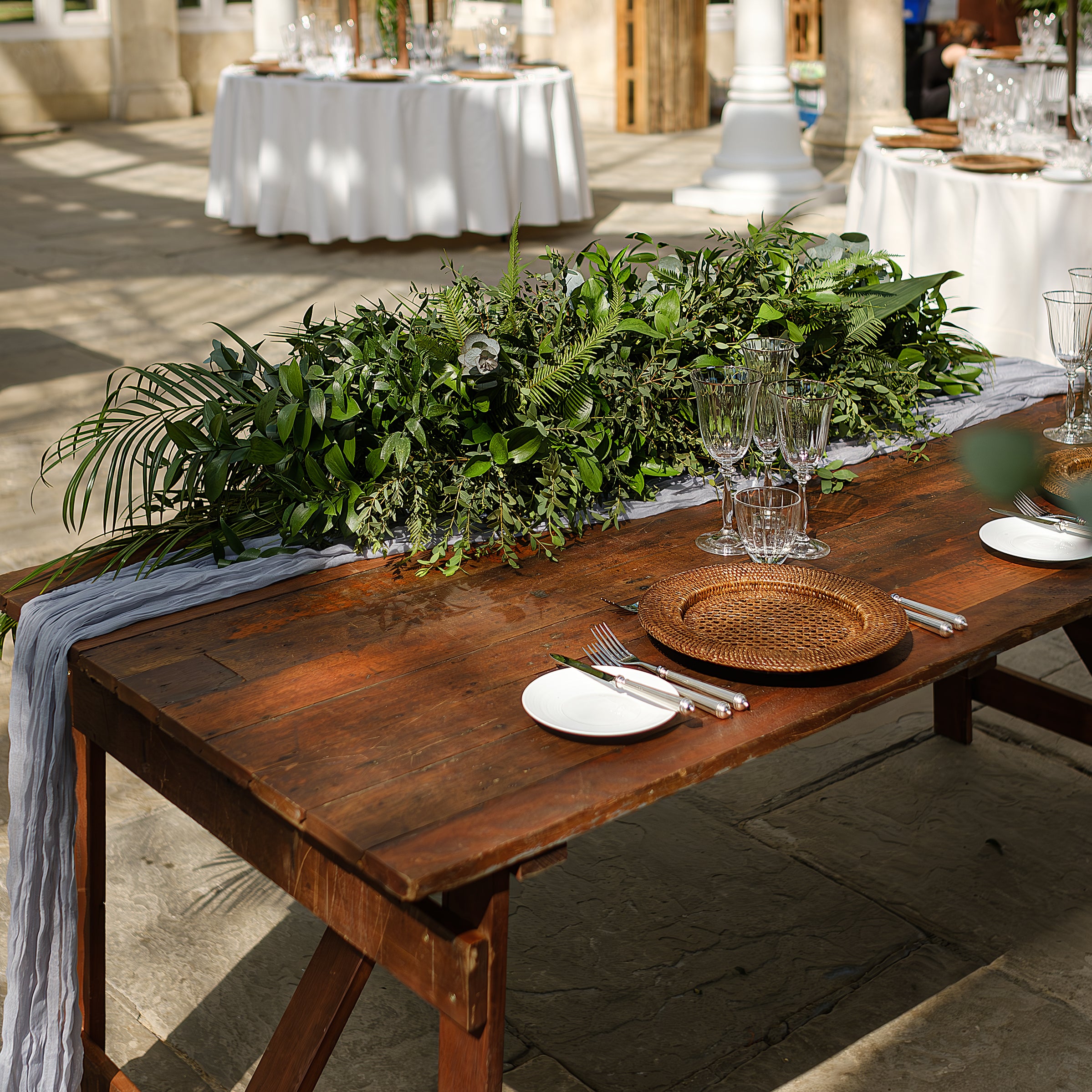 Lush green foliage table runner with mixed ferns and trailing eucalyptus on rustic wooden table at Syon Park conservatory reception - Floral Design by Amaranté London
