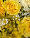 Close-up detail of golden yellow roses, cream carnations, white chamomile daisies and fluffy mimosa blossoms in sophisticated fresh flower arrangement - Amarante London