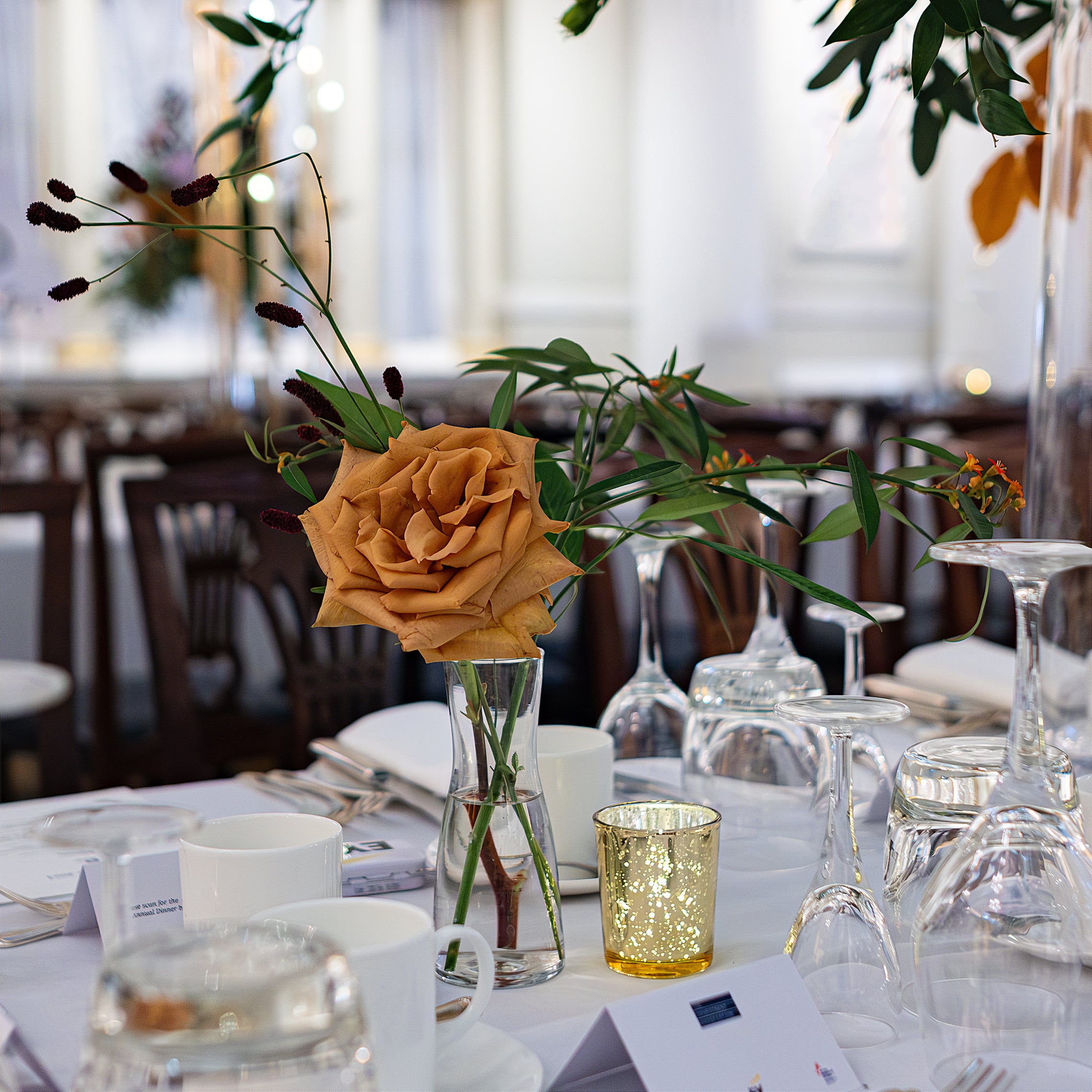 A single rose in jar placed on a large dining table