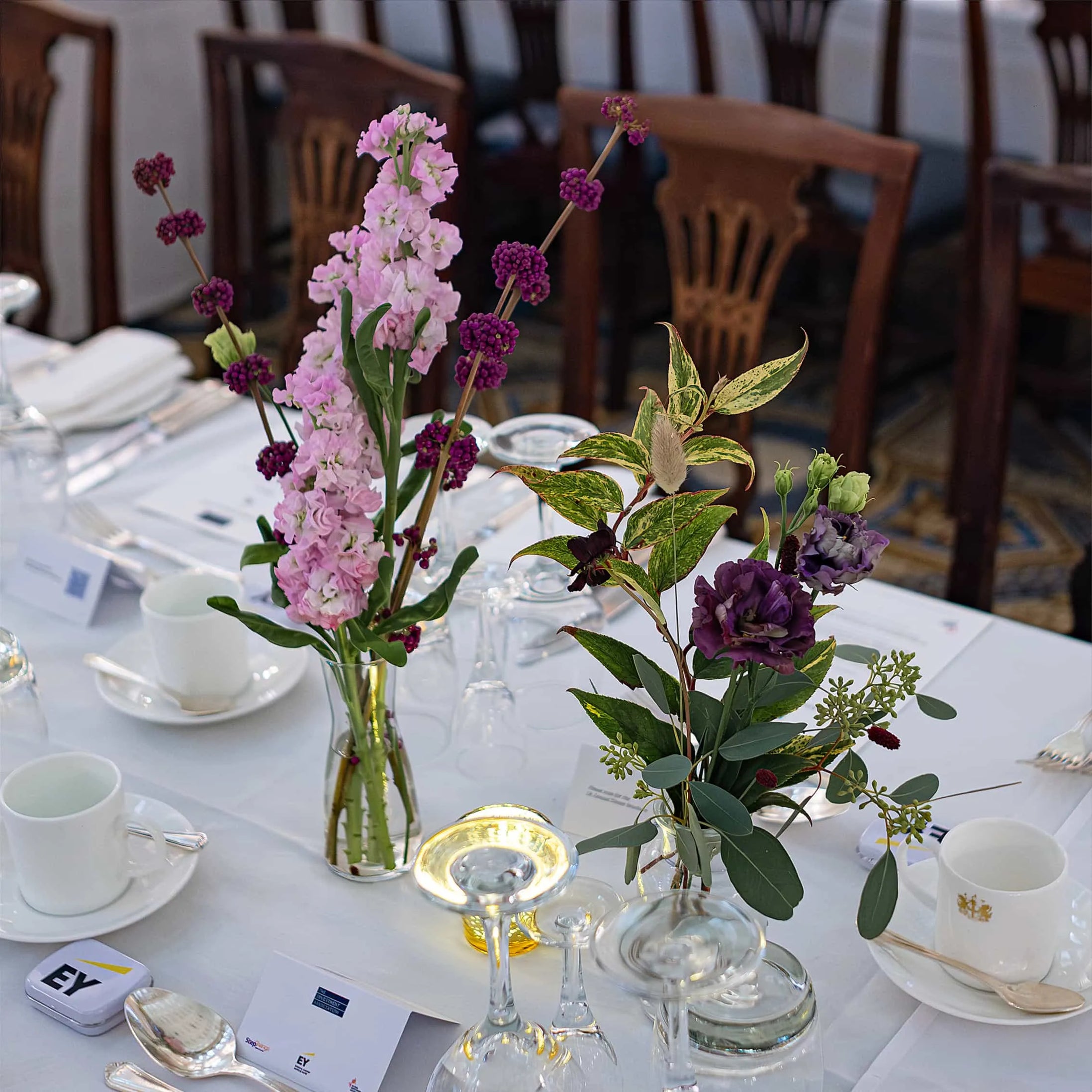 Two small floral arrangements in adjacent jars placed to be part of a table display
