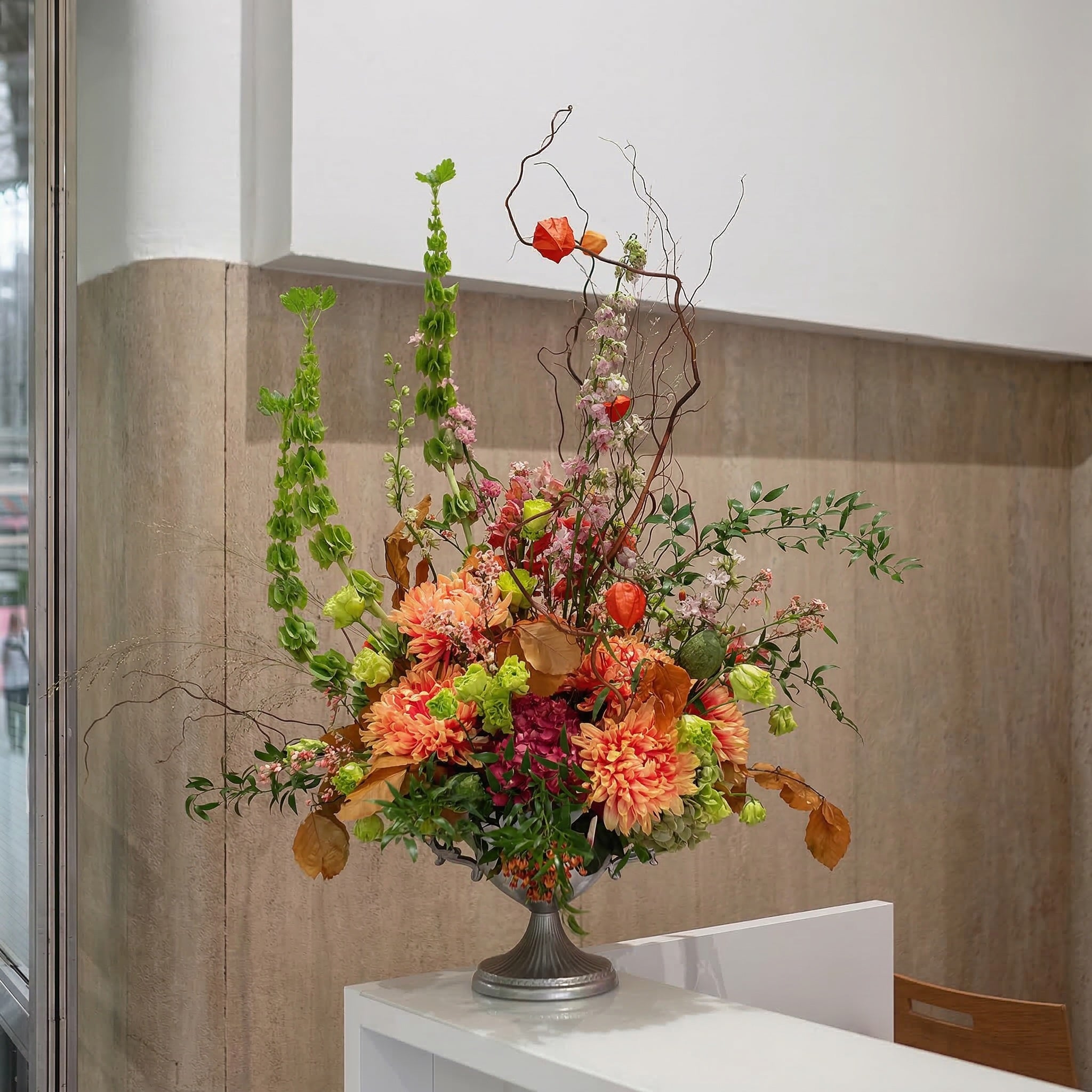 Autumn floral arrangement featuring orange dahlias, physalis and seasonal botanicals in a classic urn vase, styled for a London hotel lobby by Amarante London