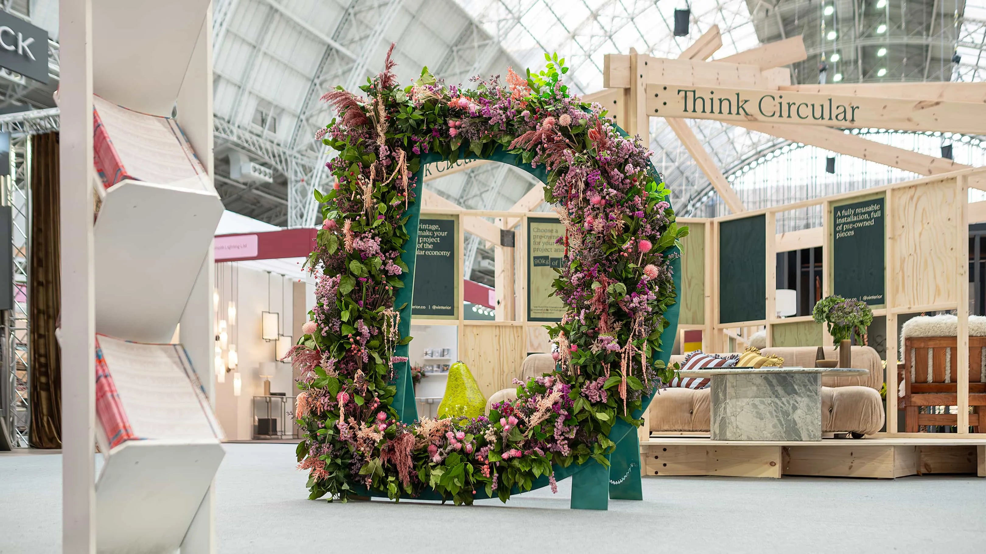 Architectural floral arch in the shape of a D, adorned with pink and green blossoms, framing a sustainable living exhibit and blending nature with design innovation - Amaranté London Event Florist