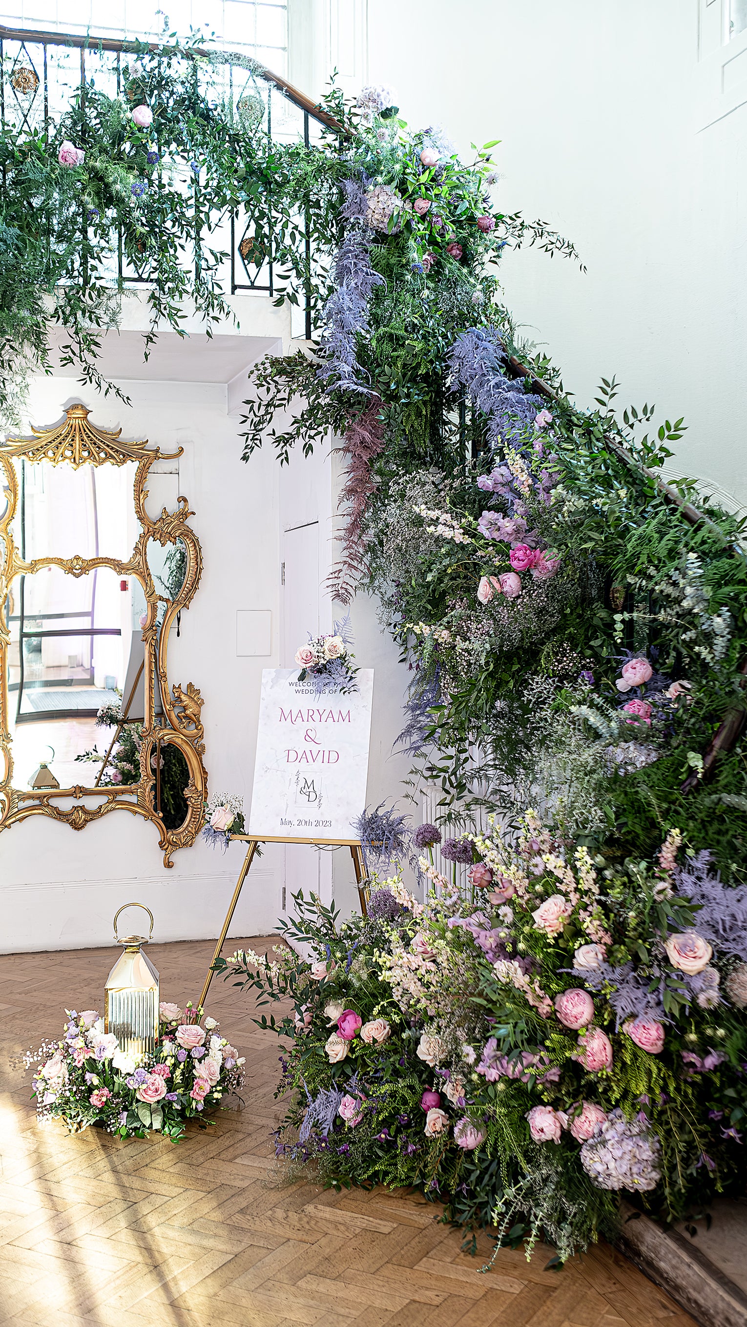 Wedding welcome display at One Marylebone with ornate gold easel, floral staircase garland, and elegant interior details - Floral Design by Amaranté London