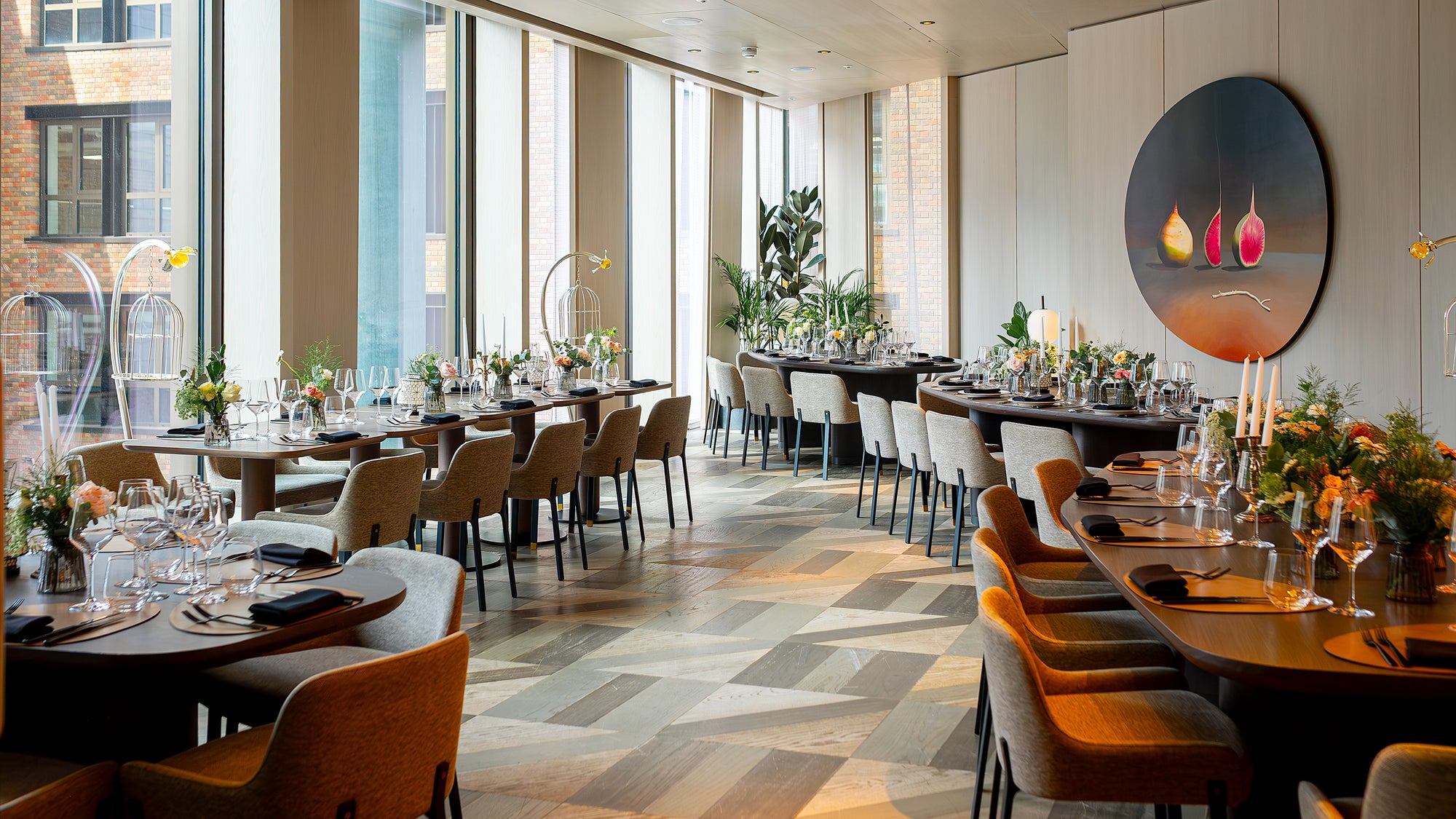 This is a view of the luxurious dining area at Pan Pacific prepared for a corporate event. It is adorned with floral arrangements designed, created, and installed by event florist Amaranté London. The flowers for this event feature a variety of blooms with lush greenery and stylish table settings, creating a sophisticated and inviting atmosphere.